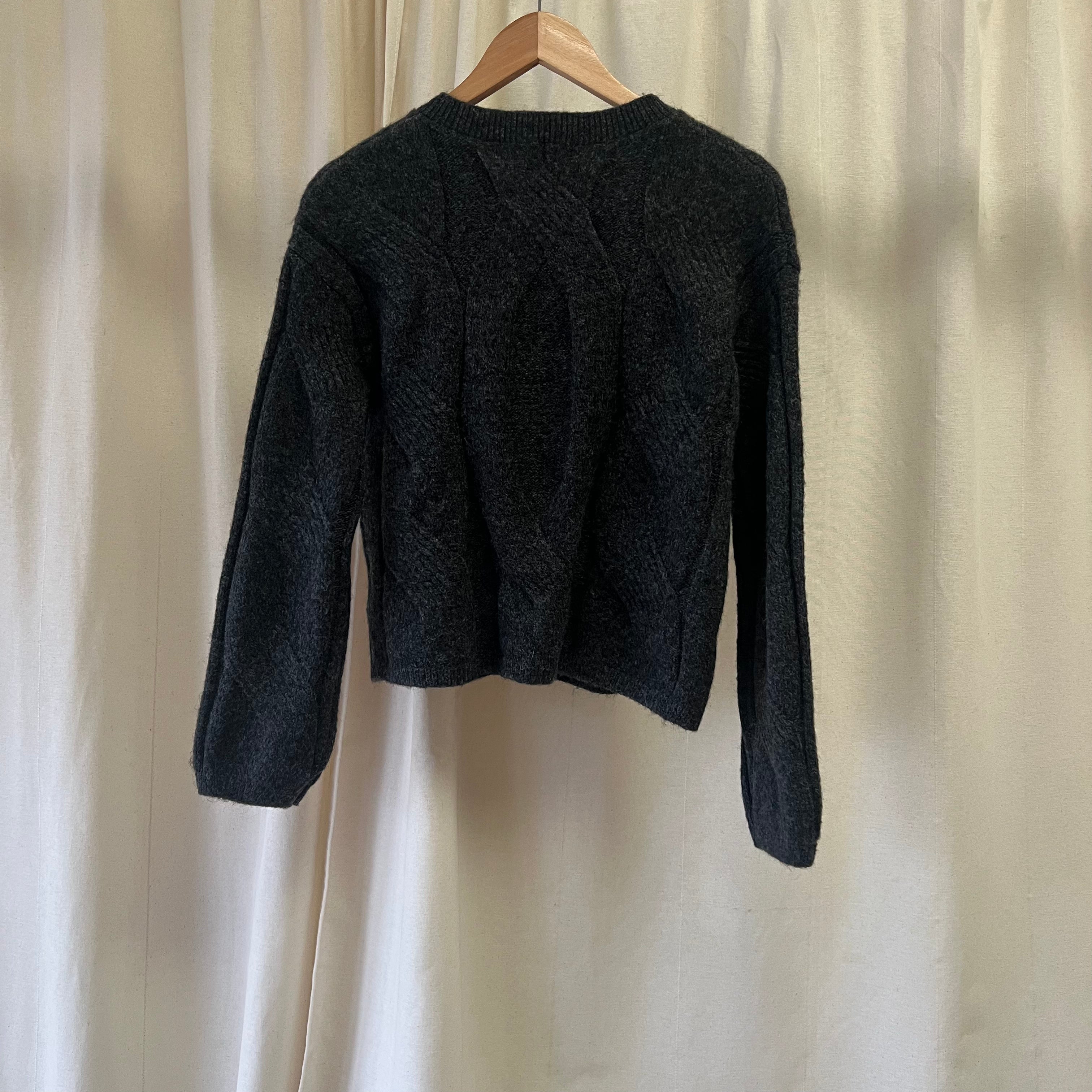 Black knitted sweater on a hanger against a beige curtain background
