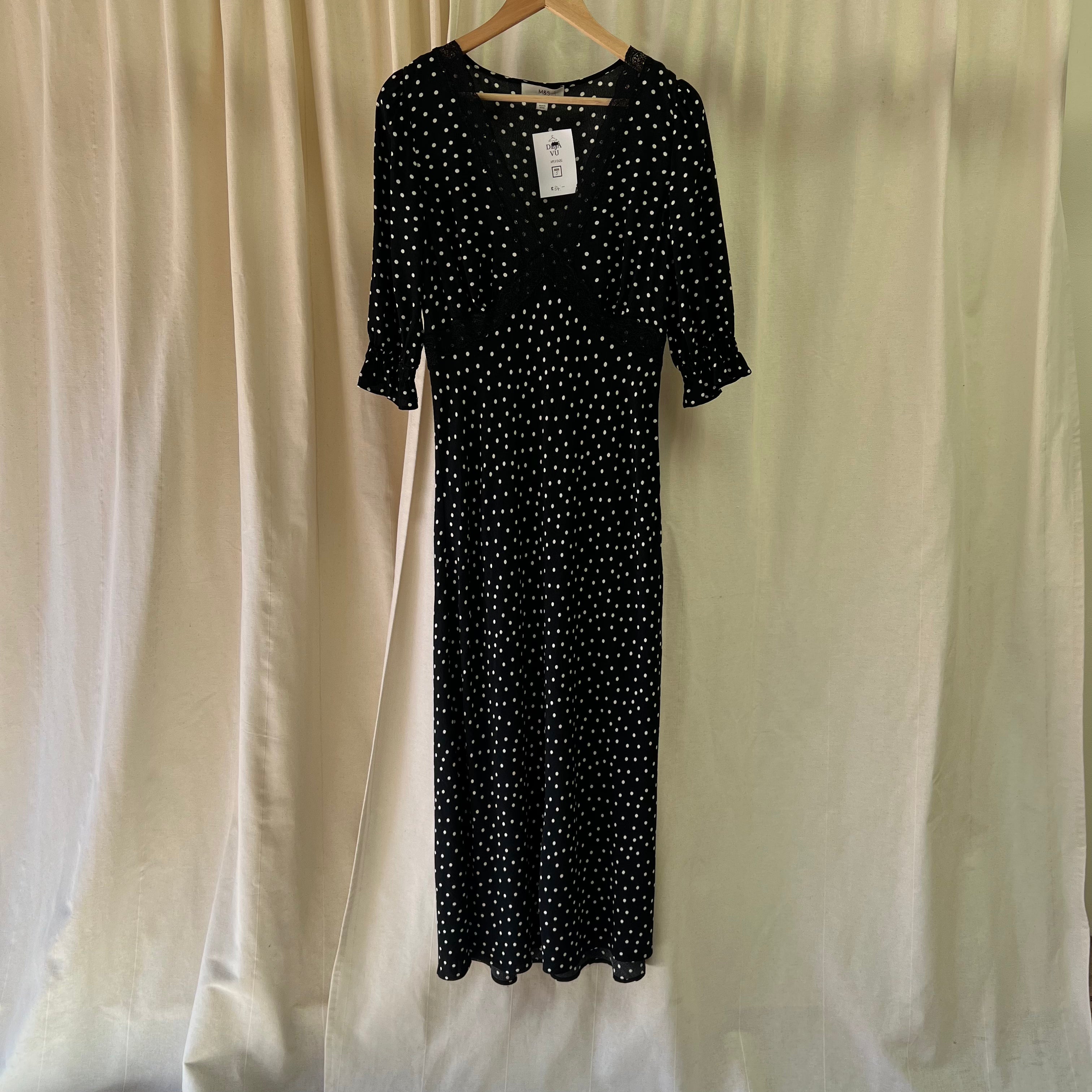 Black polka dot dress on a hanger against a beige curtain background