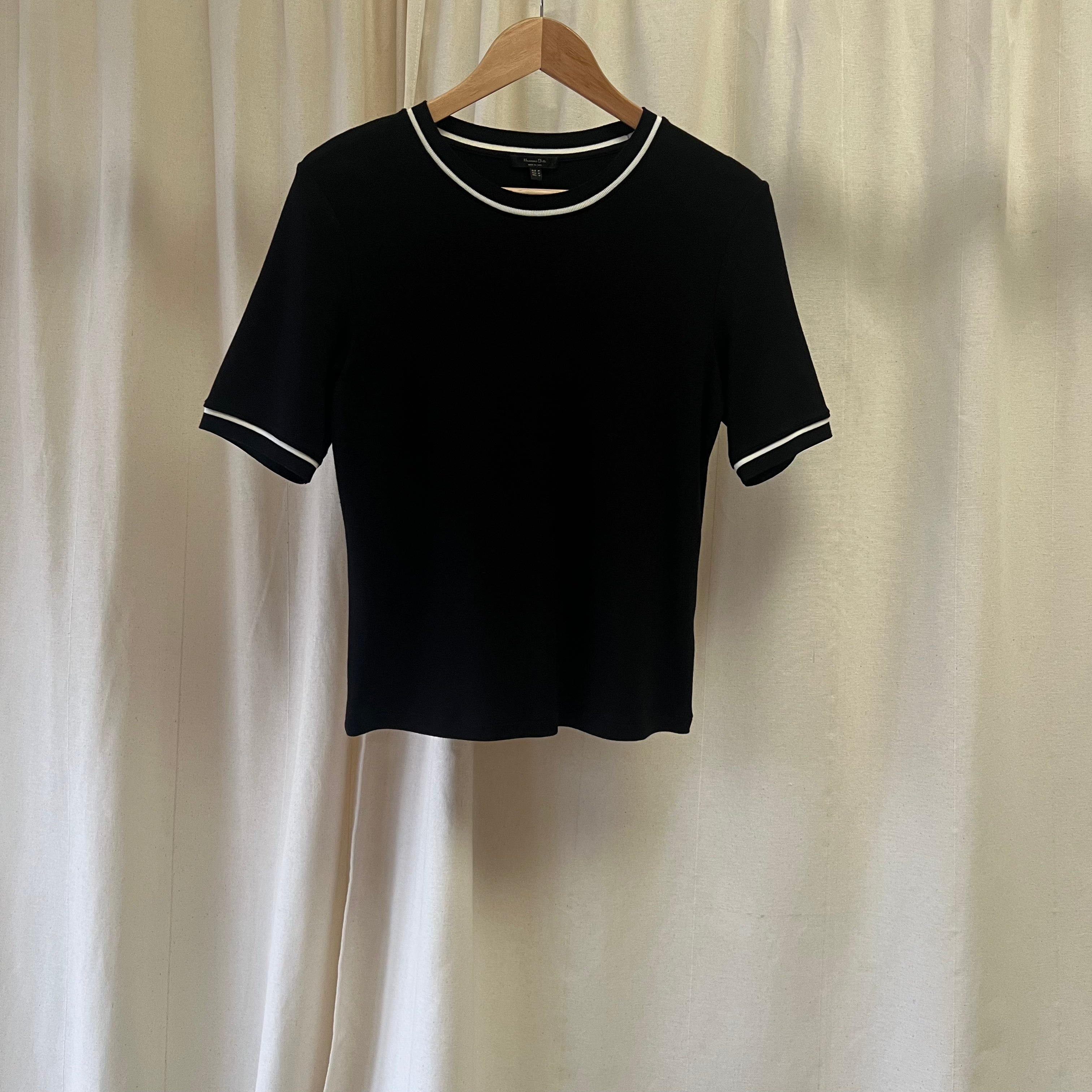 Black t-shirt with white trim on a hanger against a beige curtain background