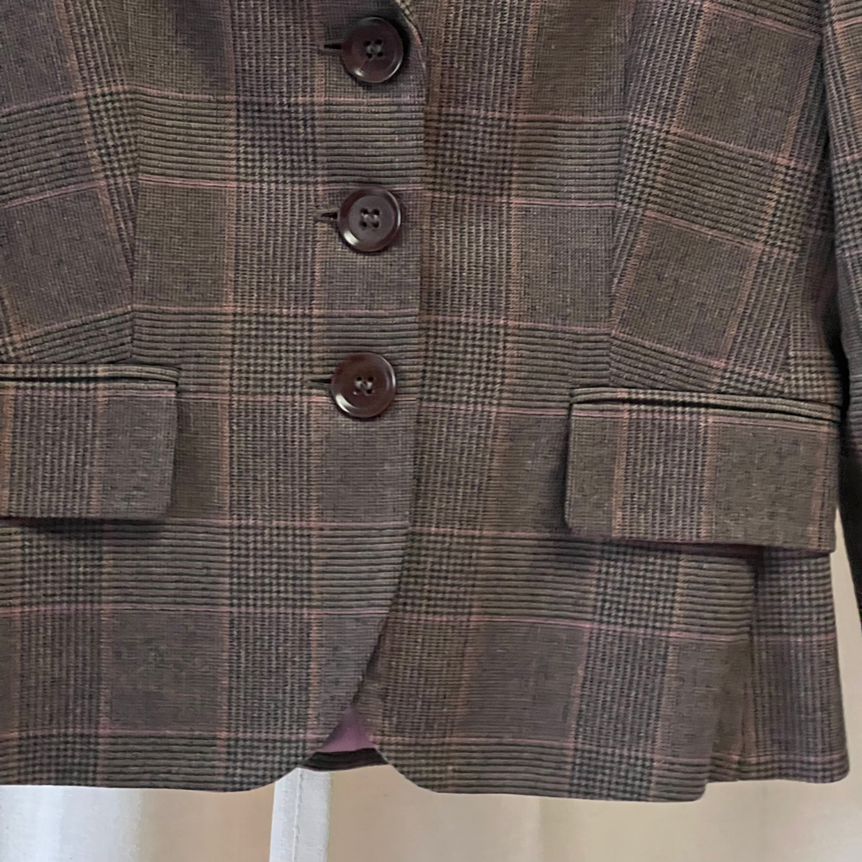Close-up of a brown plaid blazer with buttons and pockets on a white background