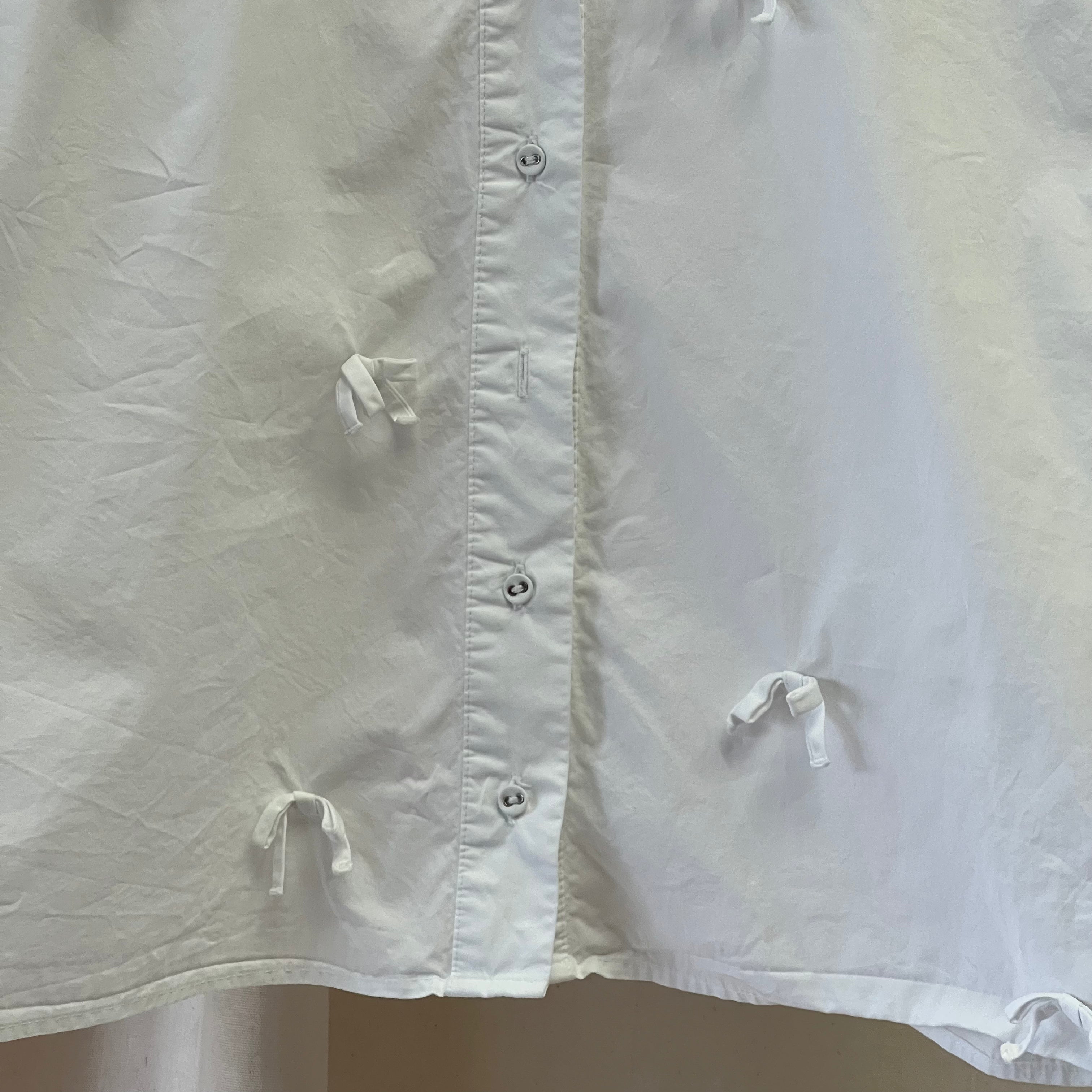 Close-up of a light-colored shirt with buttons and drawstrings on a neutral background