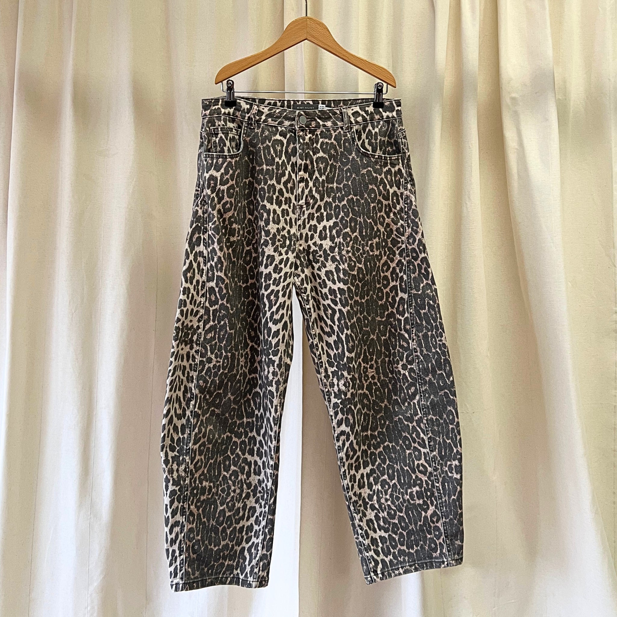 Leopard print pants on a hanger against a beige curtain background