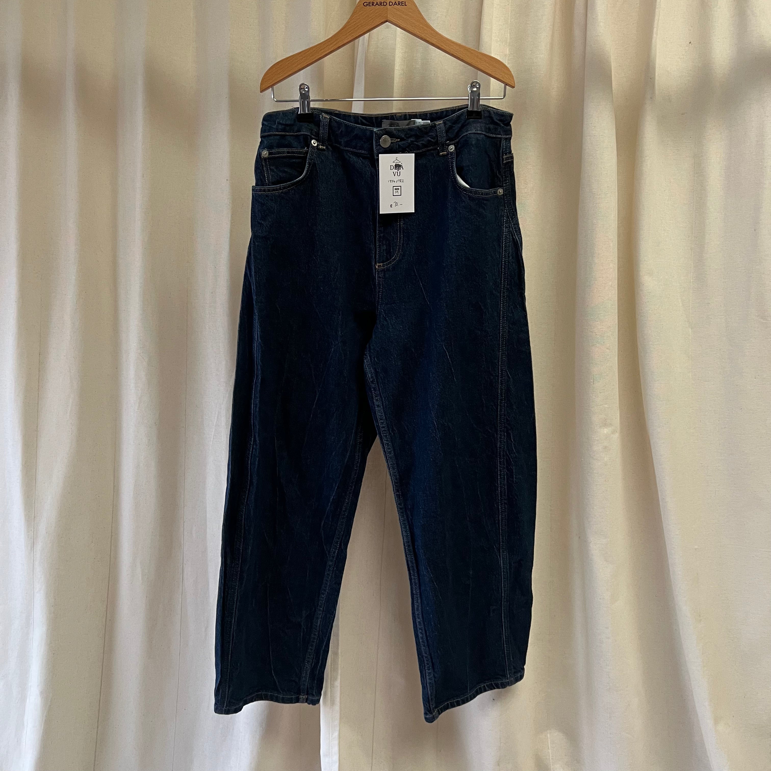 Dark blue jeans on a hanger against a beige curtain background