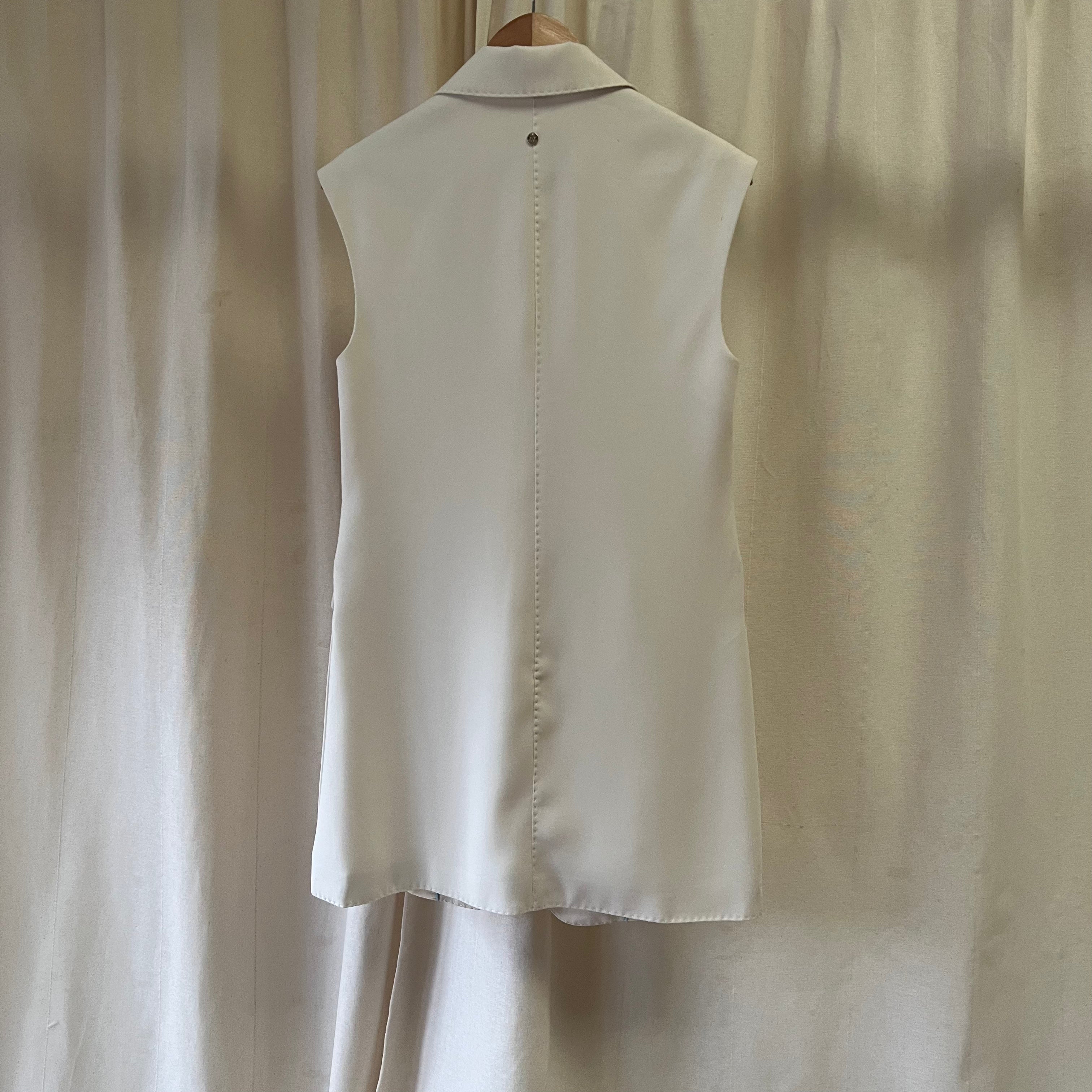 Beige sleeveless shirt on a hanger against a beige curtain background