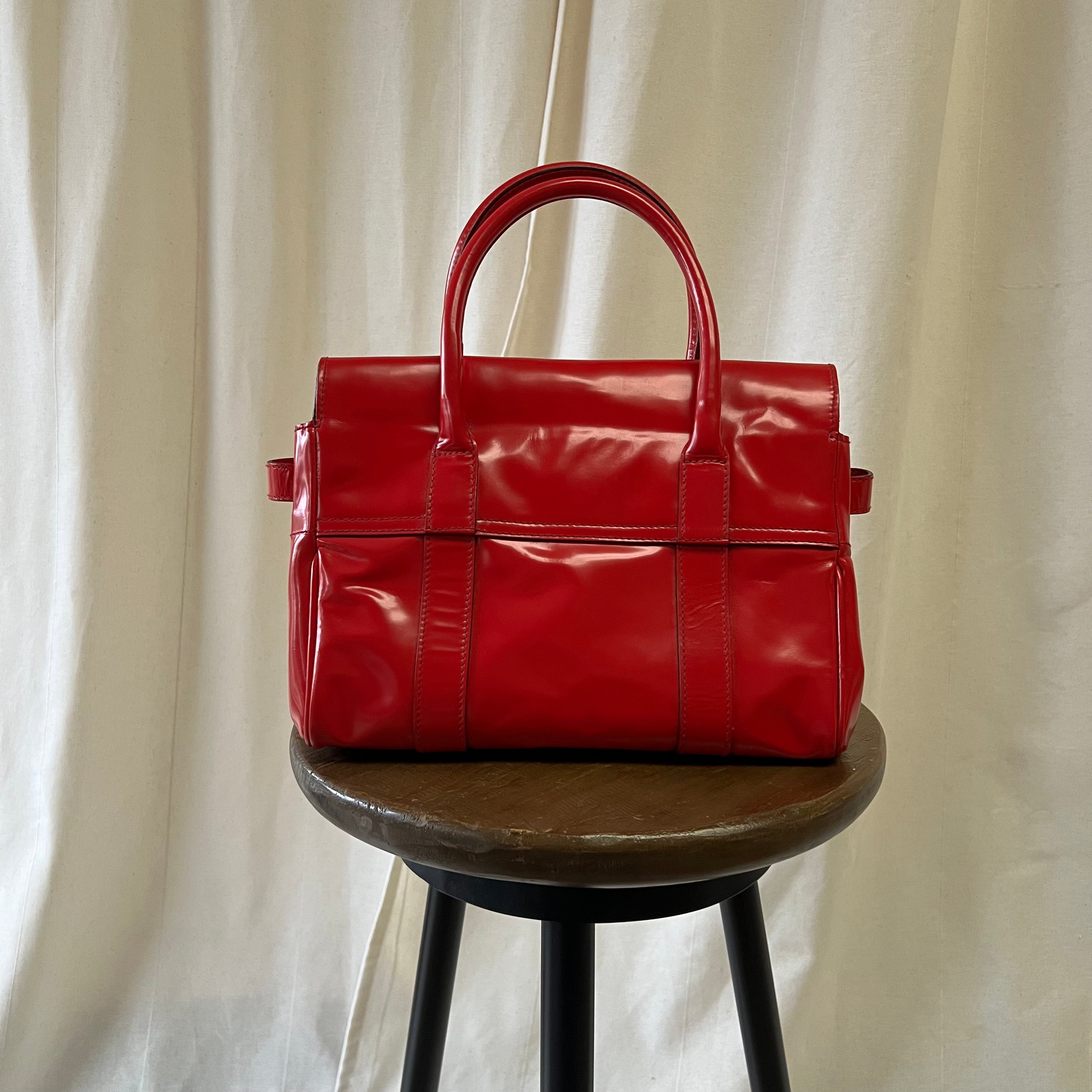 Red handbag on a wooden stool against a beige curtain background
