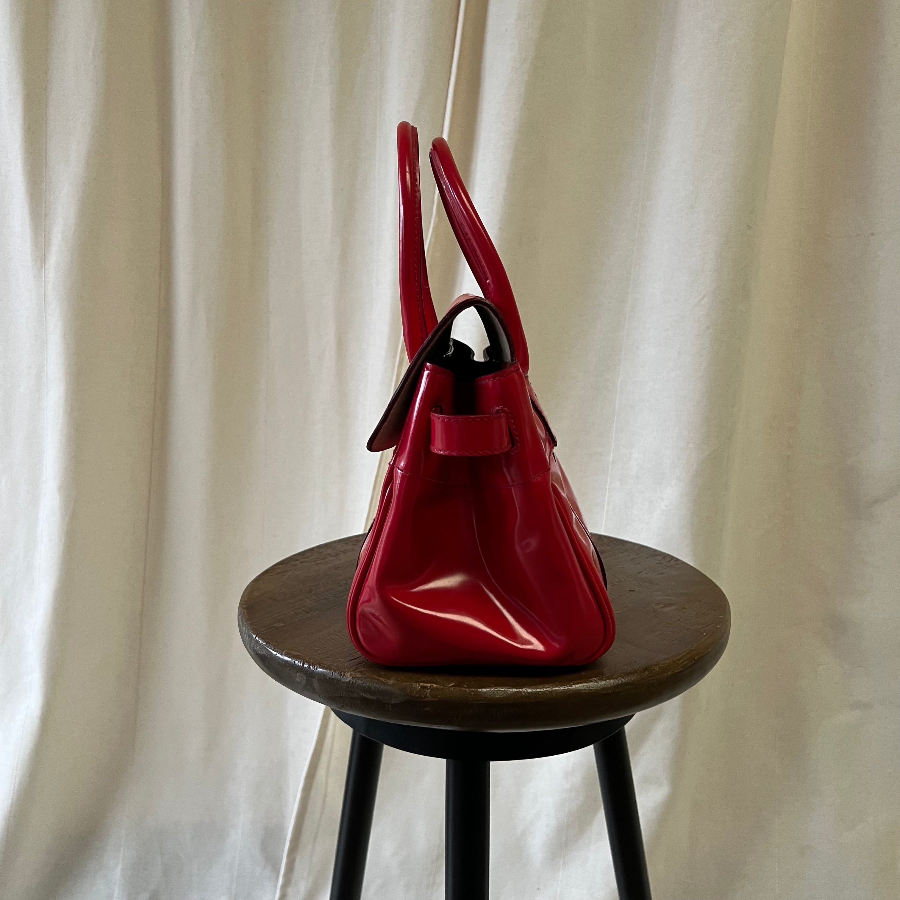 Red handbag on a wooden stool against a white curtain background