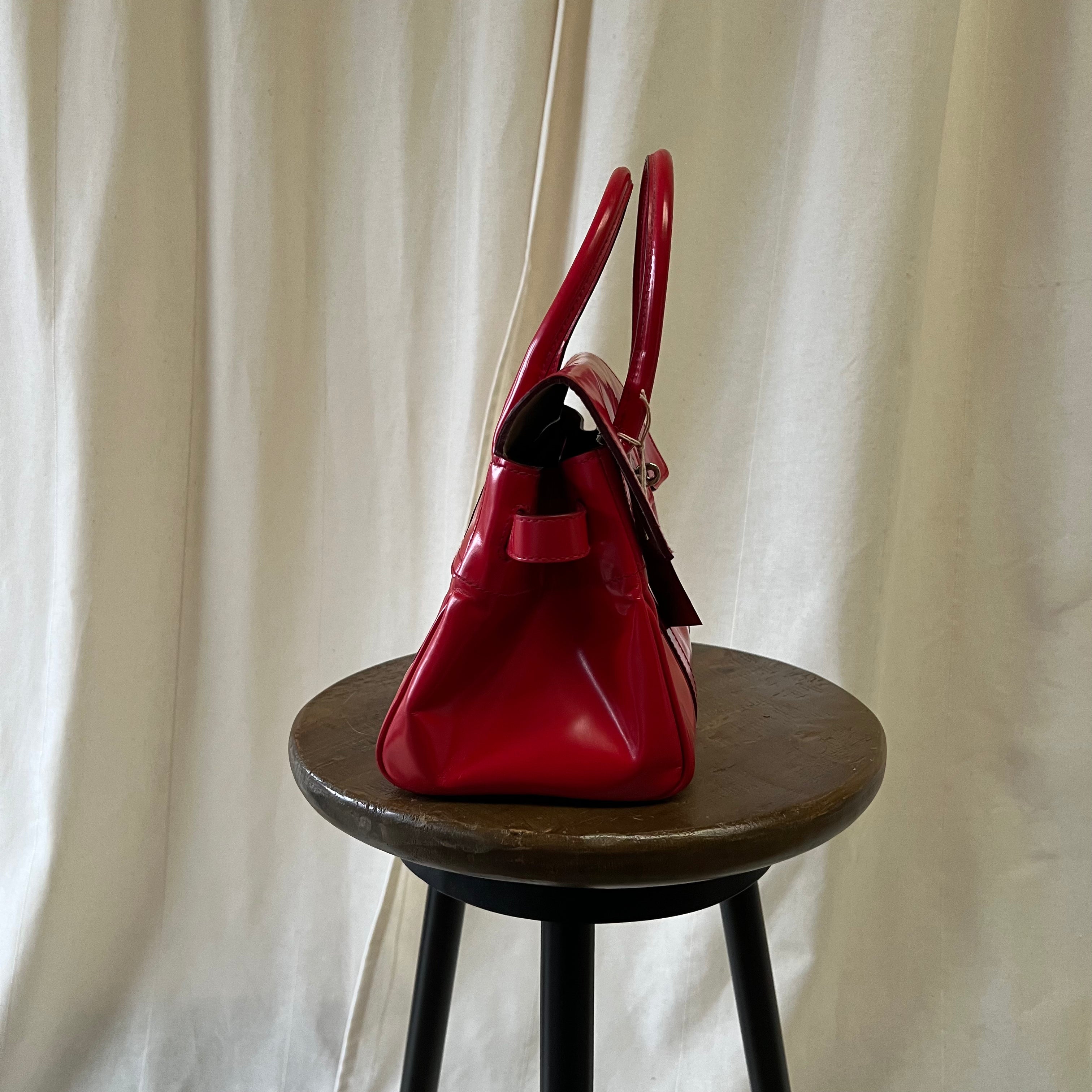 Red handbag on a wooden stool against a white curtain background
