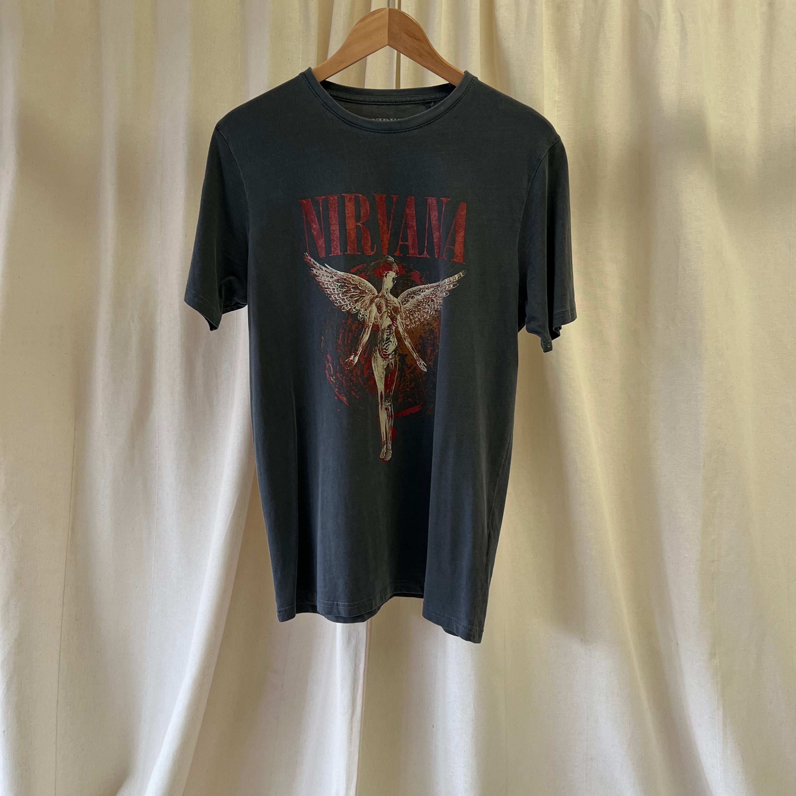 Nirvana t-shirt with graphic design on a hanger against a beige curtain background