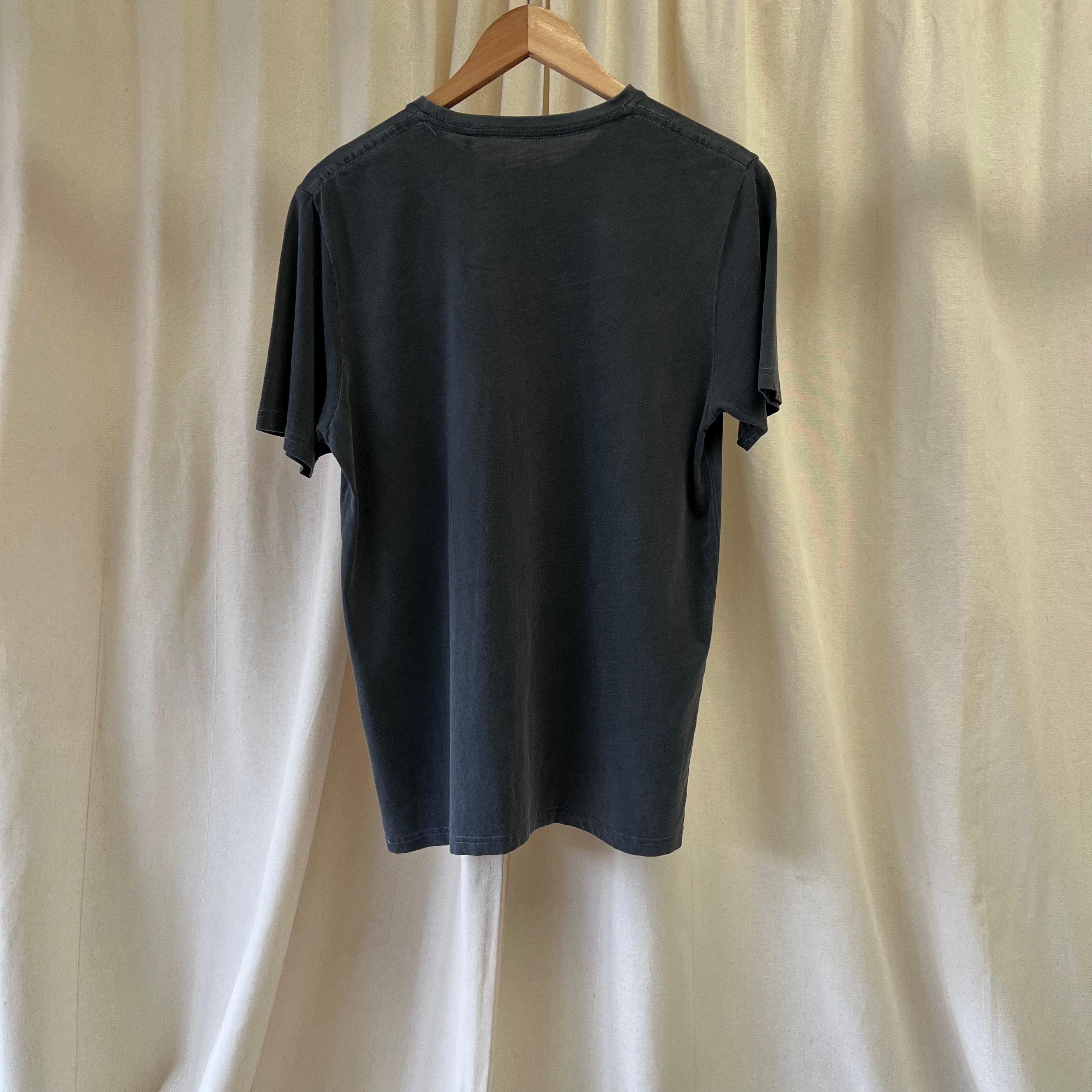 Black t-shirt on a wooden hanger against a beige curtain background