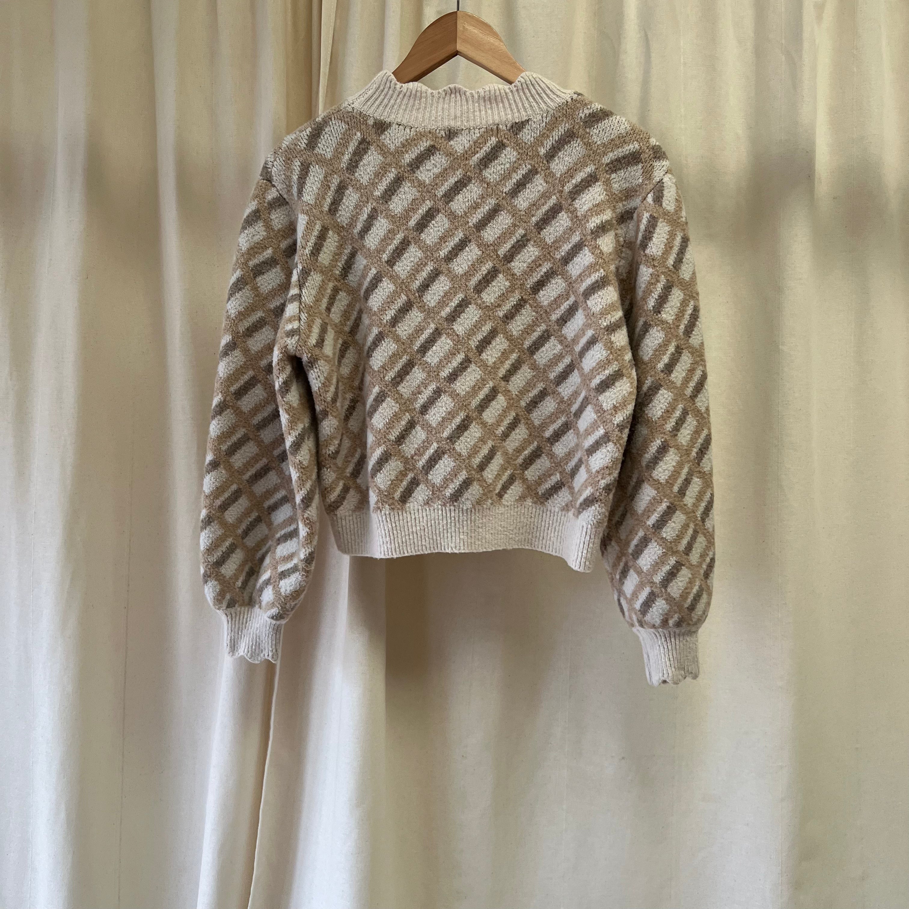 Knitted sweater with a geometric pattern on a hanger against a neutral background