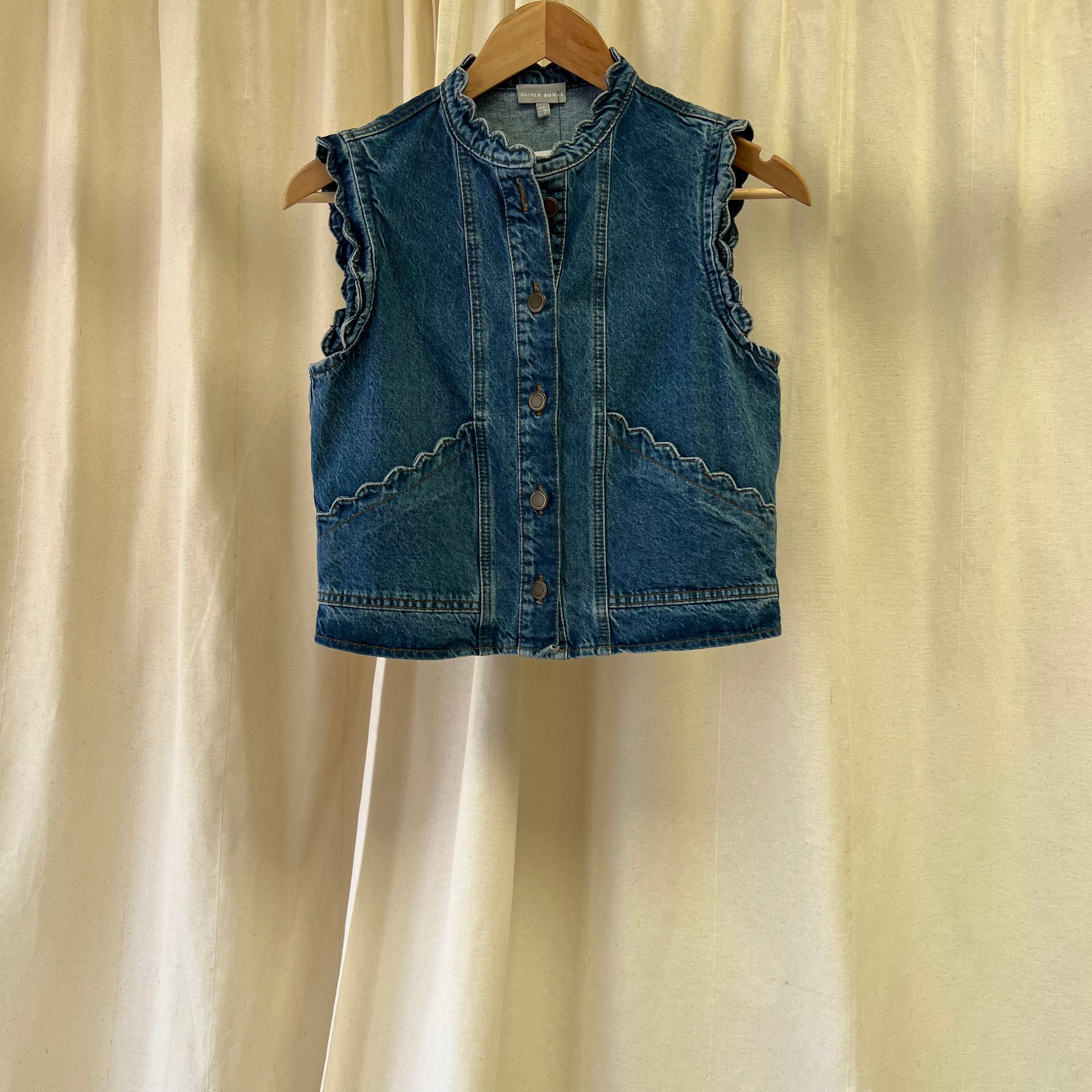 Blue denim vest on a hanger against a beige curtain background