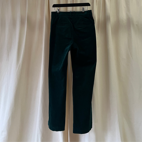Teal pants hanging on a hanger against a white curtain background