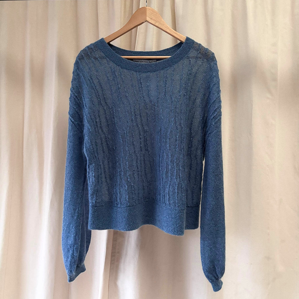 Blue sweater on a wooden hanger against a beige curtain background
