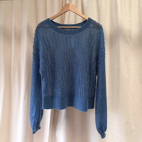 Blue sweater on a wooden hanger against a beige curtain background