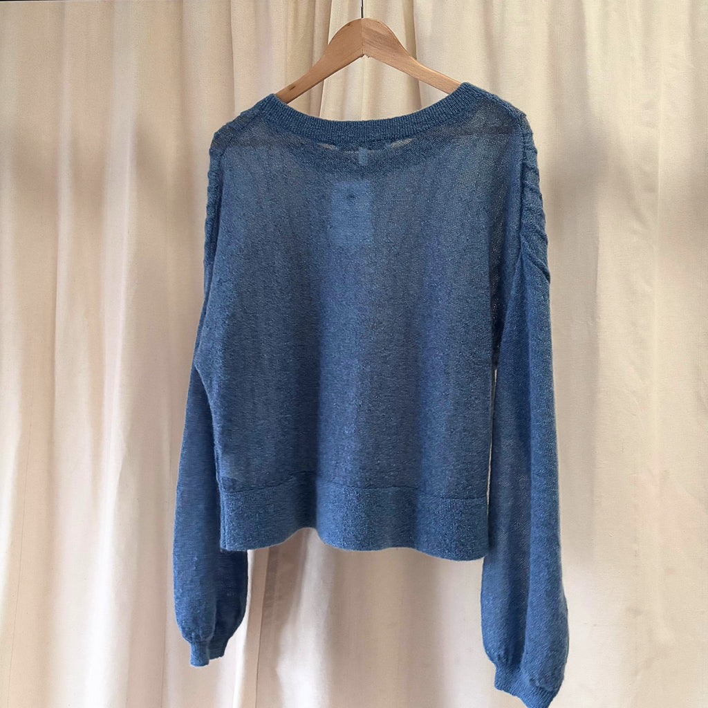 Blue sweater on a wooden hanger against a beige curtain background
