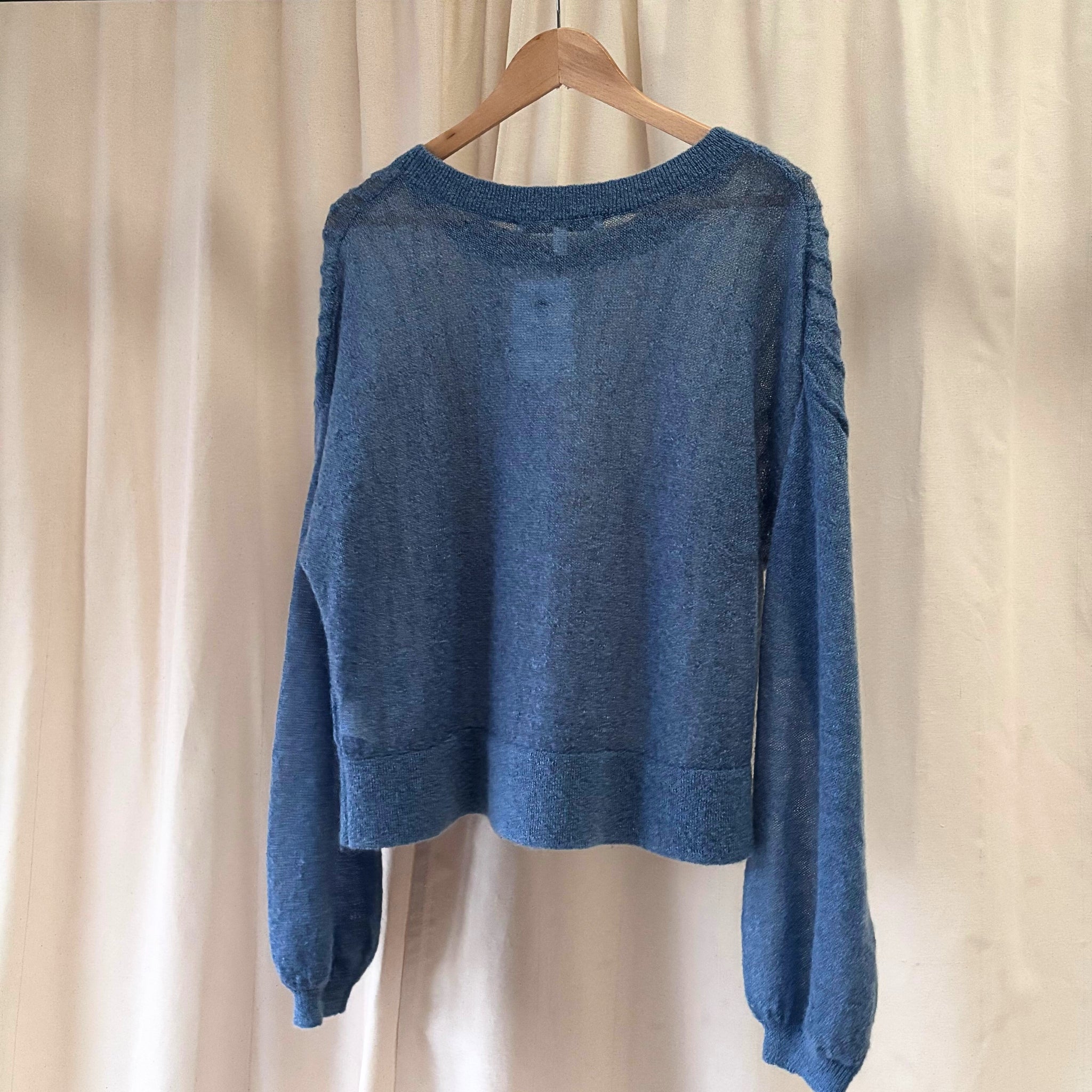 Blue sweater on a wooden hanger against a beige curtain background