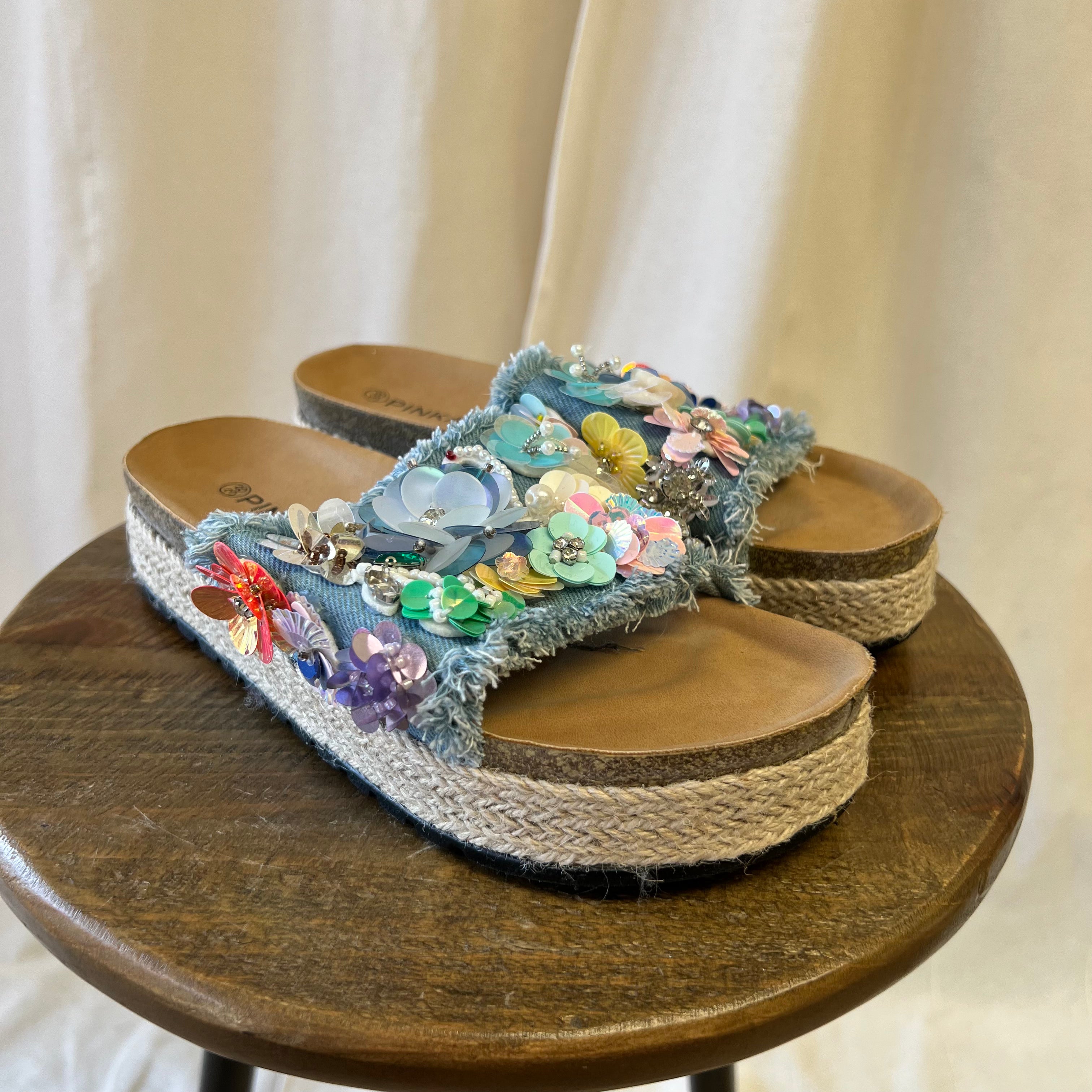 Decorative sandals with floral embellishments on a wooden stool.