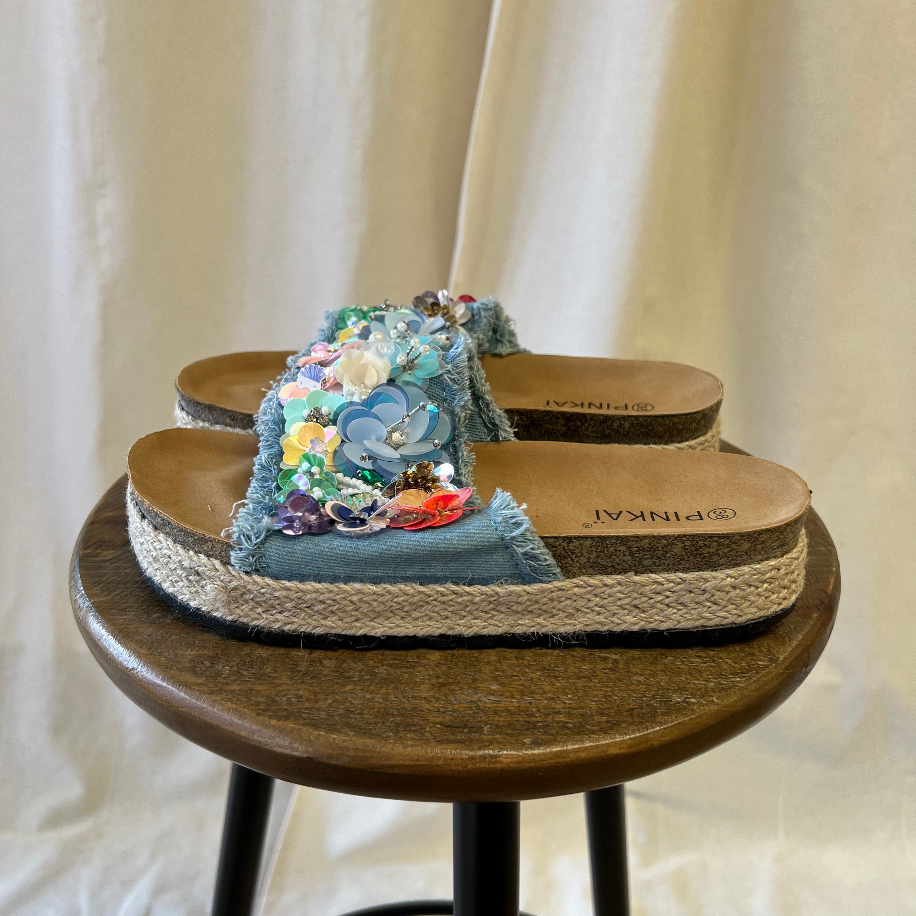 Decorative sandal with floral embellishments on a wooden stool against a neutral background
