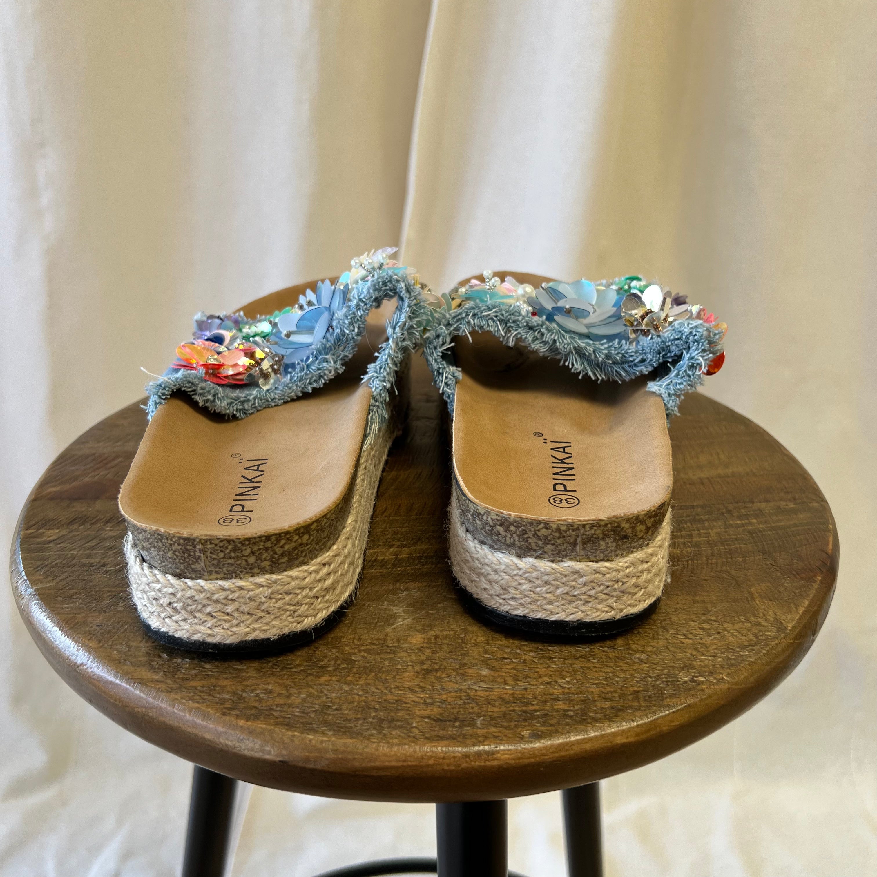 Pair of sandals with floral decorations on a wooden stool against a neutral background