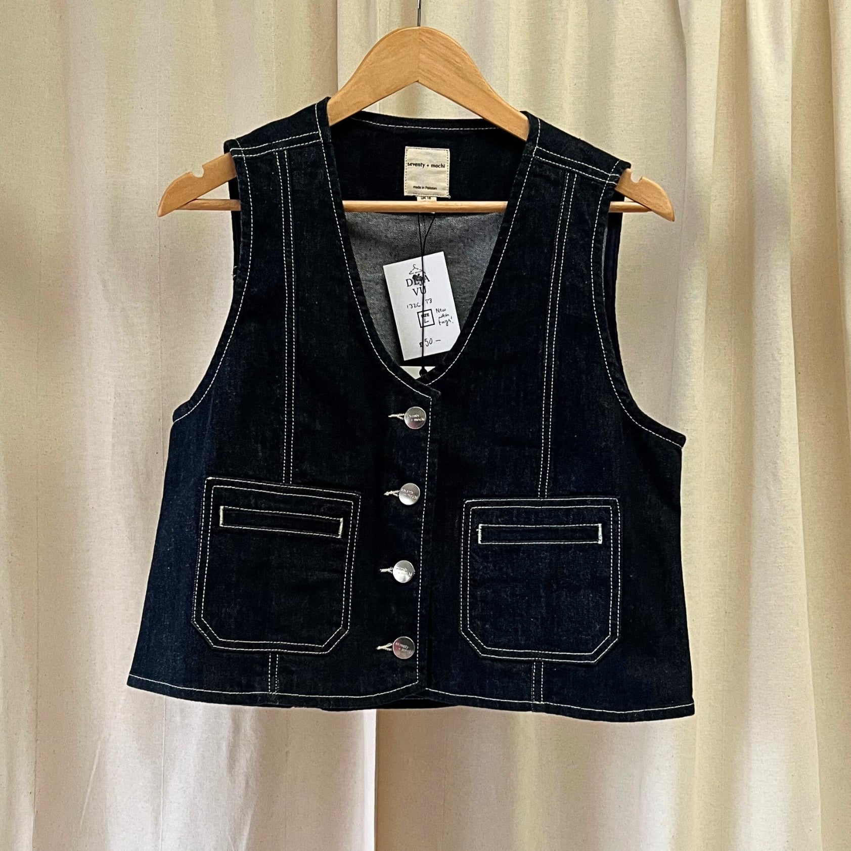 Black denim vest on a hanger against a beige curtain background