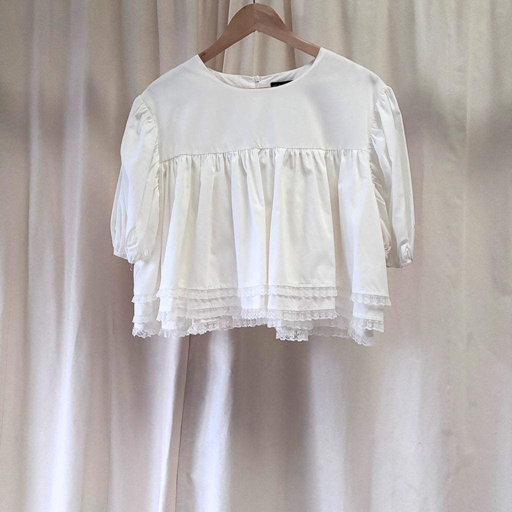 White blouse with ruffled details on a wooden hanger against a plain background