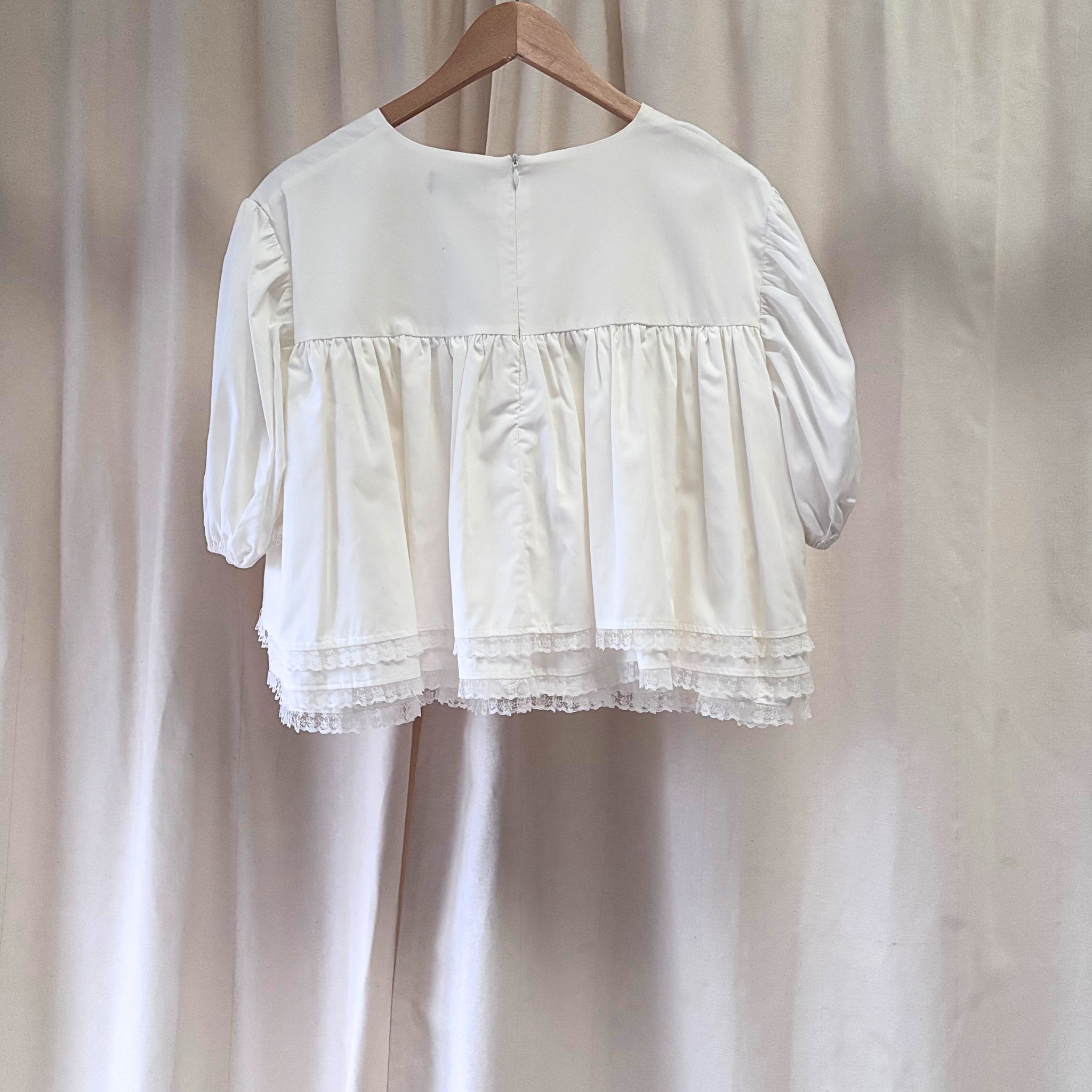 White blouse with lace details on a wooden hanger against a plain background