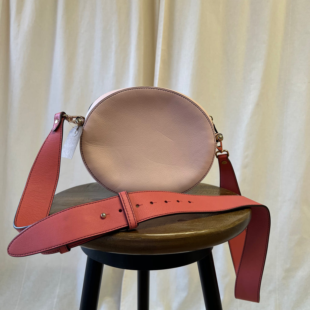 Brown leather handbag with red strap on a wooden stool against a white curtain background