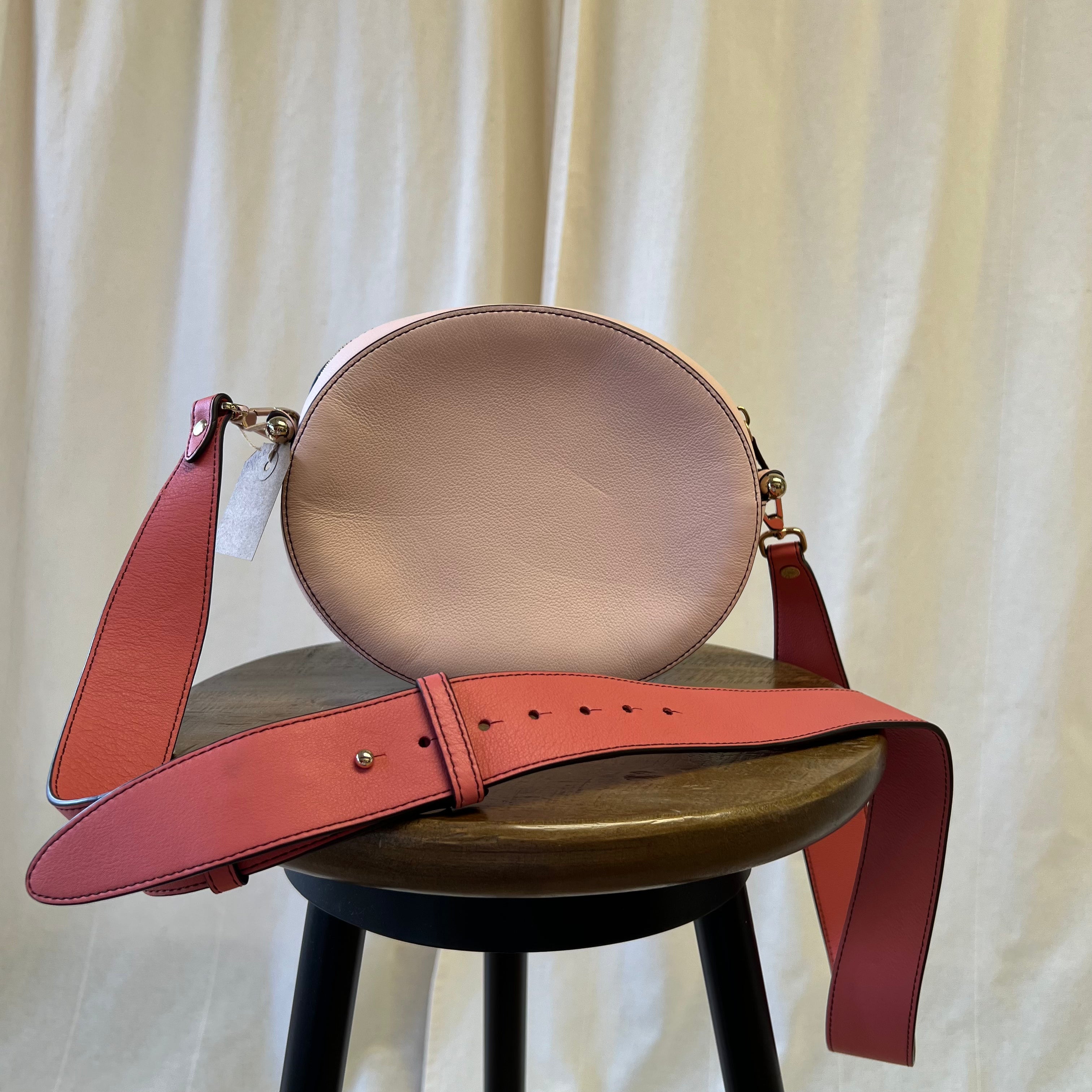 Brown leather handbag with red strap on a wooden stool against a white curtain background