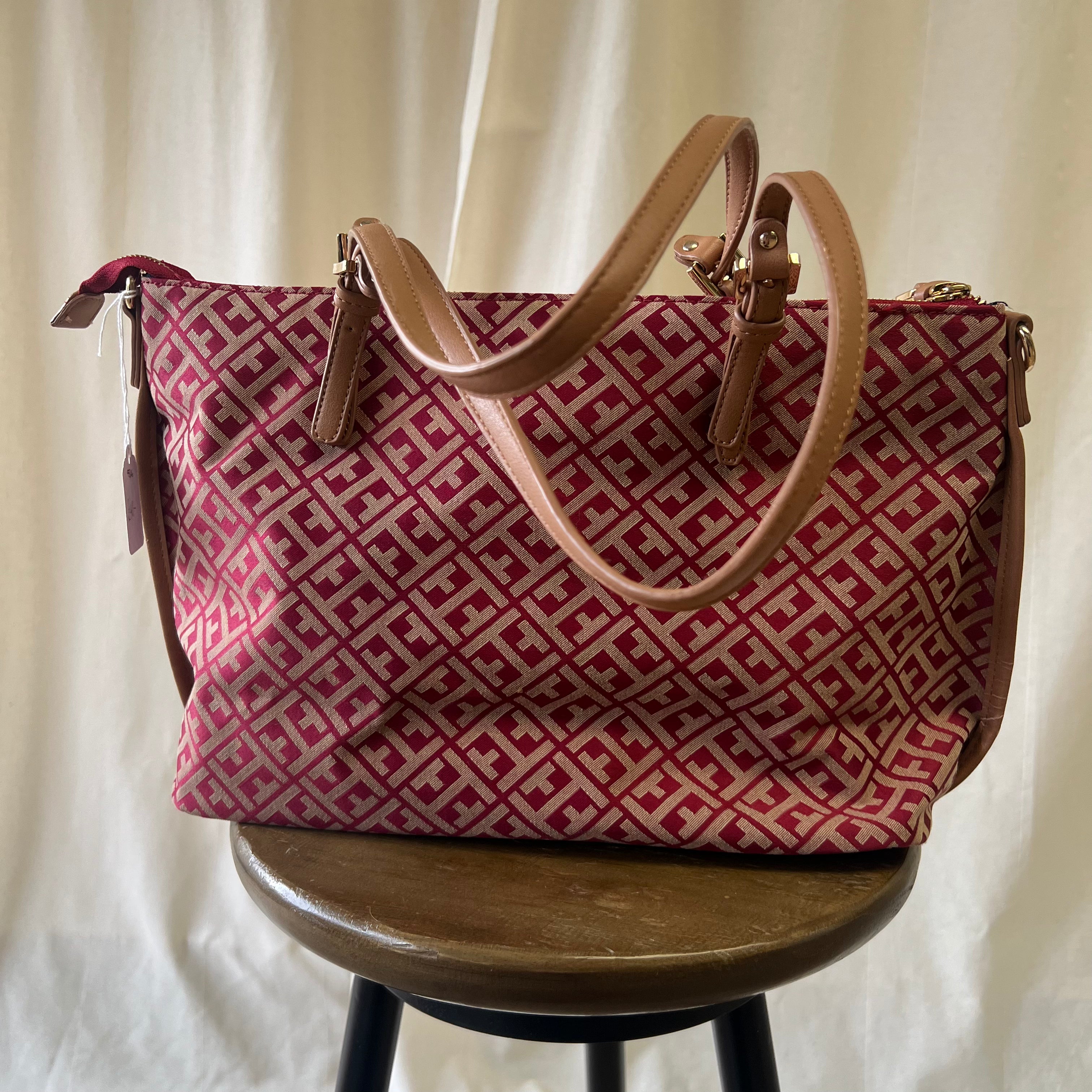 Red and beige patterned handbag on a wooden stool against a white background