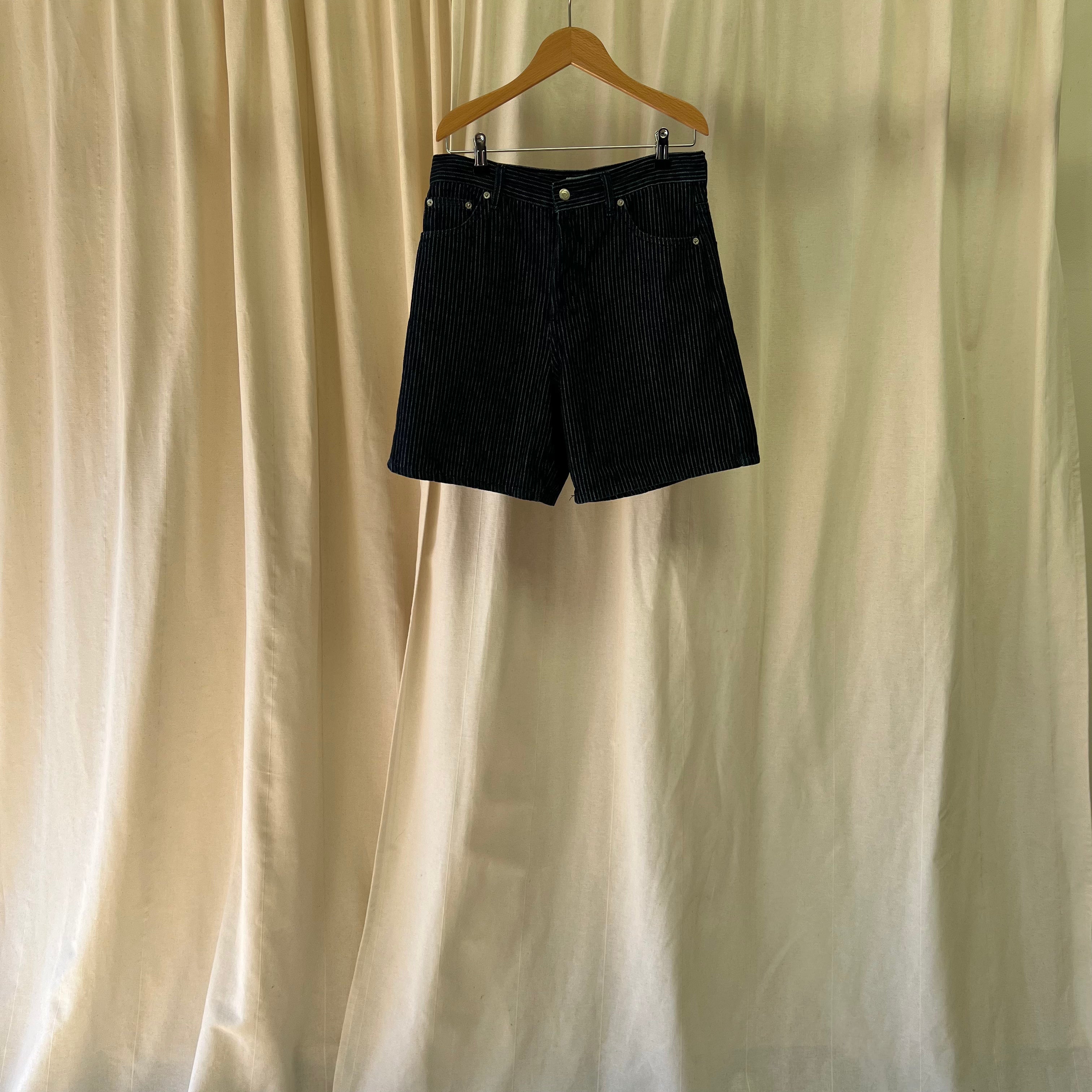 Black shorts on a hanger against a beige curtain background