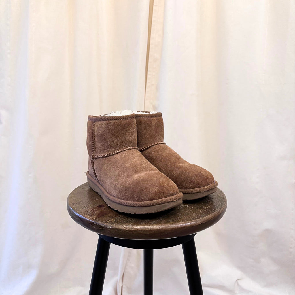 Pair of brown suede boots on a wooden stool against a white background