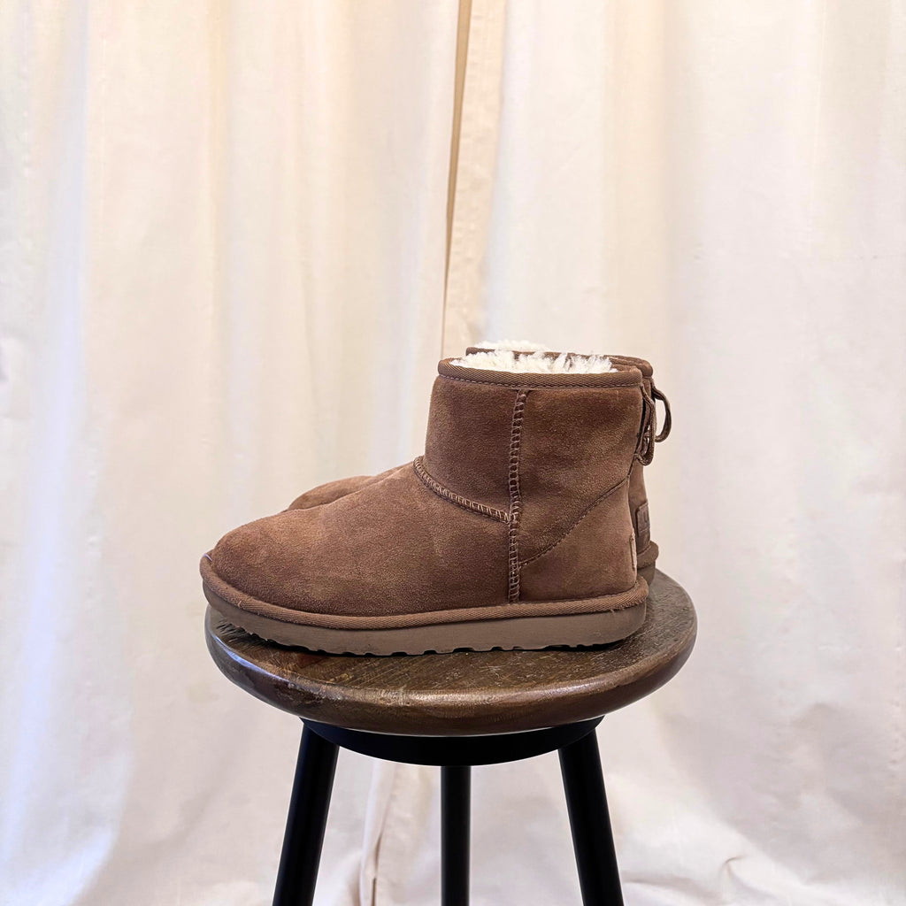 Brown suede boot on a small round stool against a white curtain background