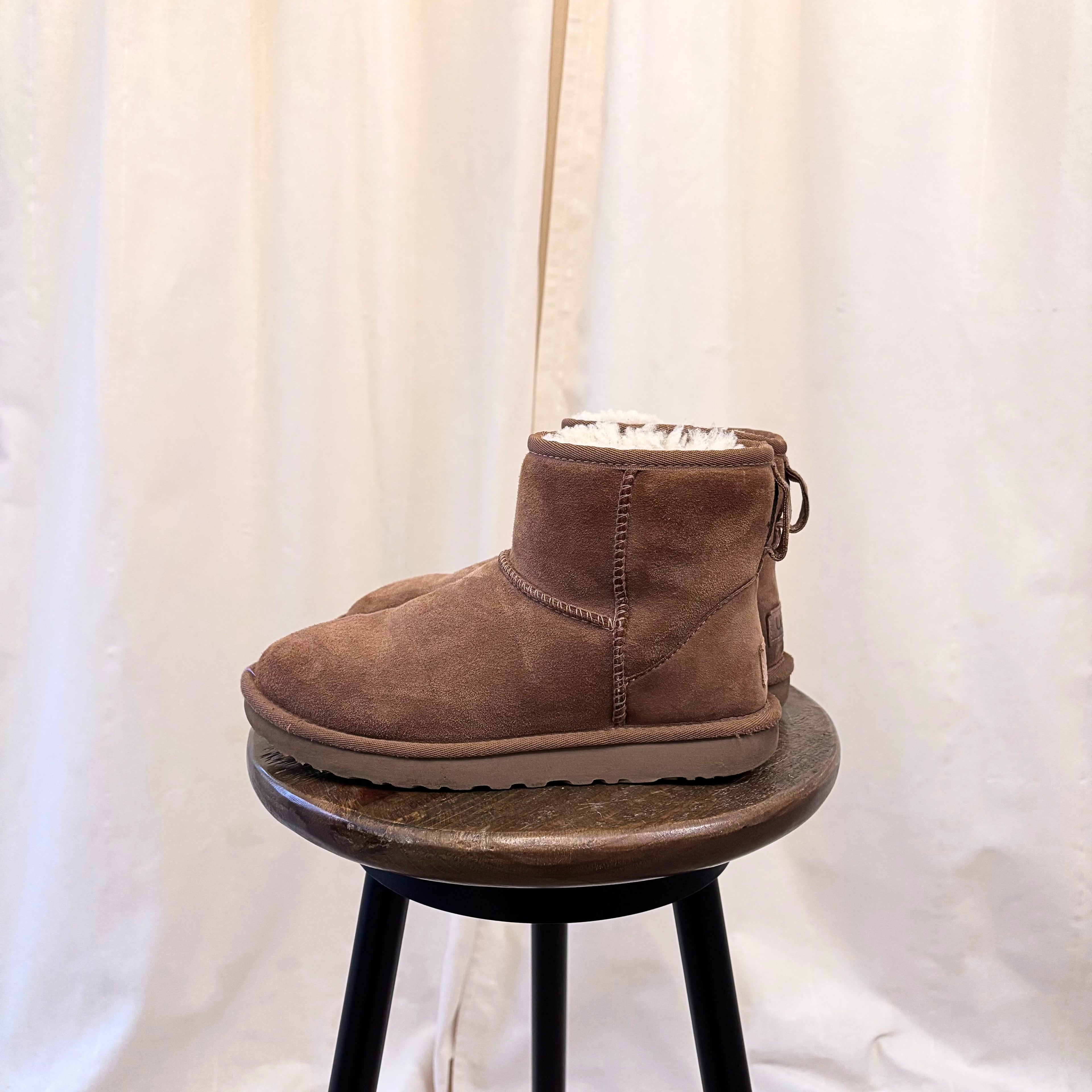 Brown suede boot on a small round stool against a white curtain background