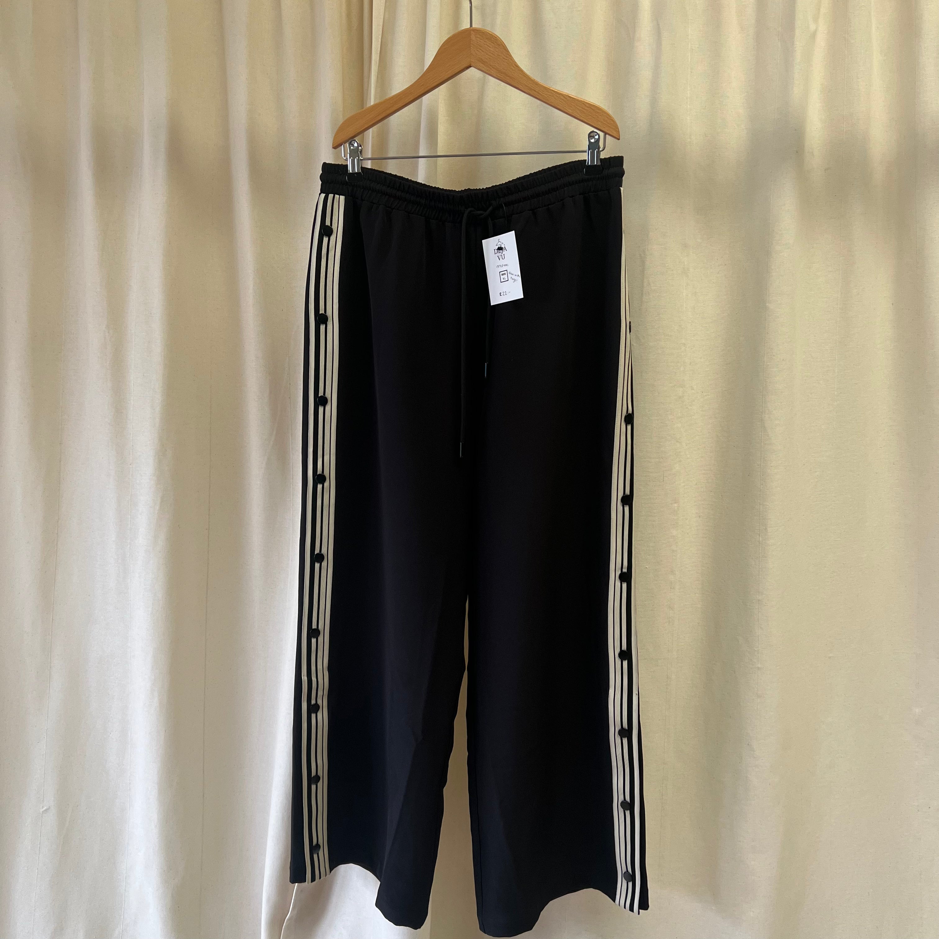 Black pants with white stripes on a hanger against a beige curtain background