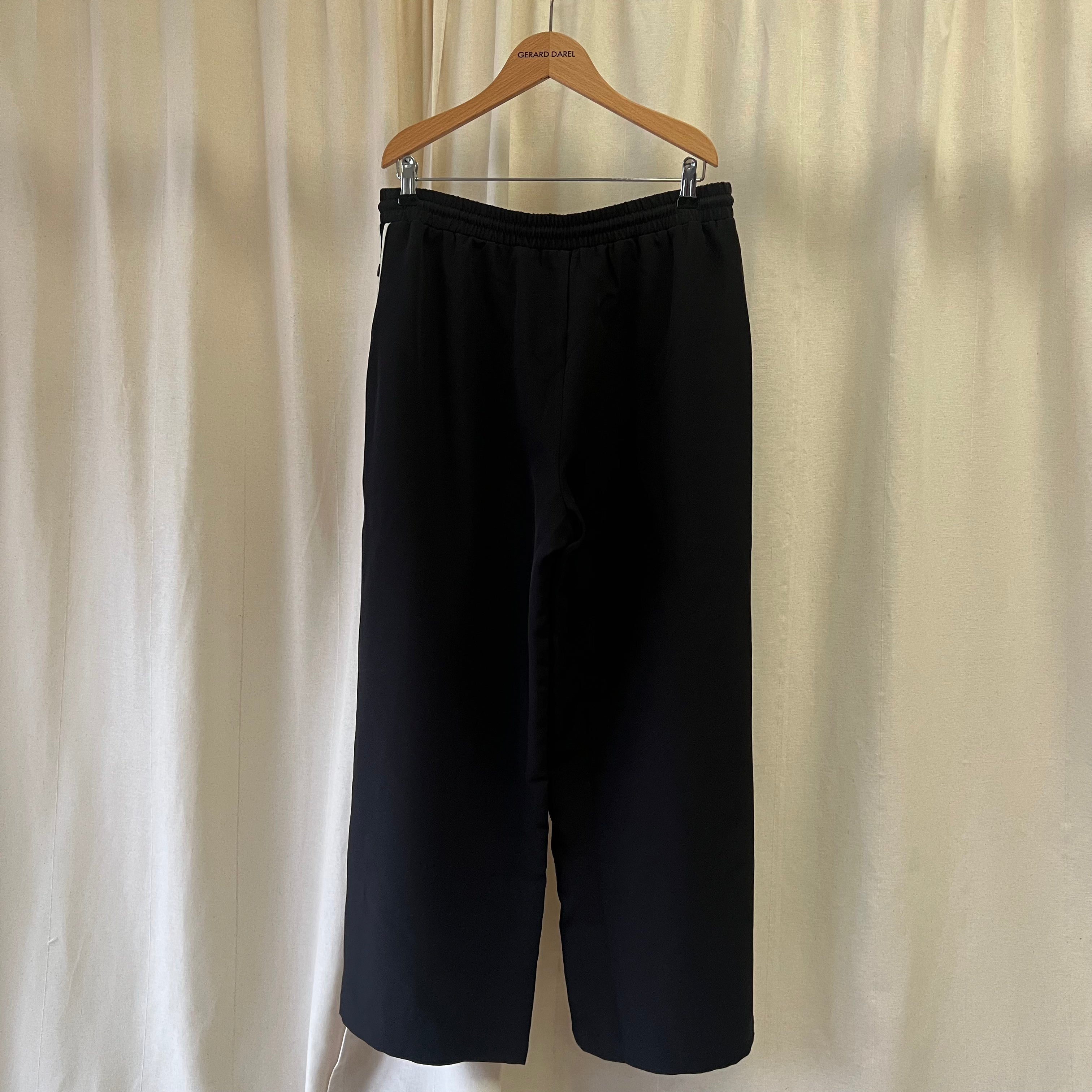 Black pants on a wooden hanger against a beige curtain background