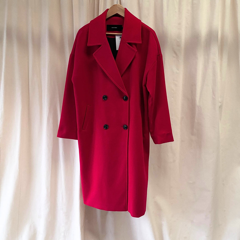 Red coat on a hanger against a beige curtain background