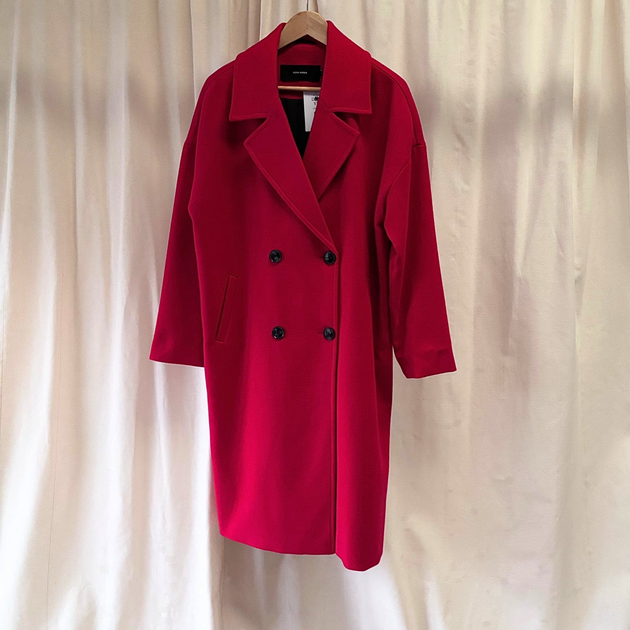 Red coat on a hanger against a beige curtain background