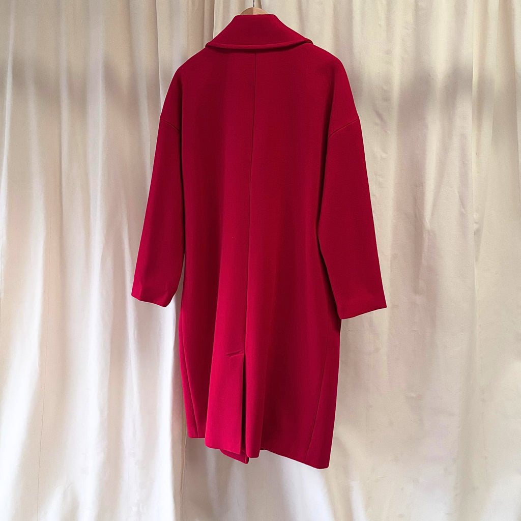 Red coat on a hanger against a beige curtain background