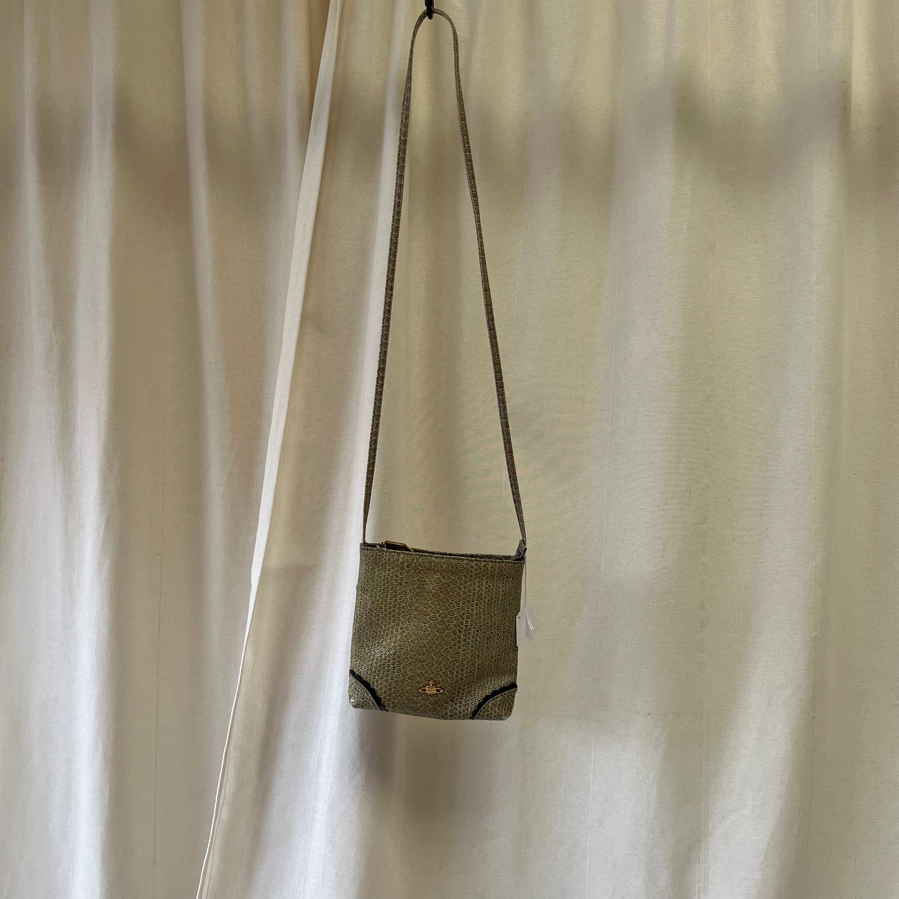 Small green handbag hanging against a white curtain