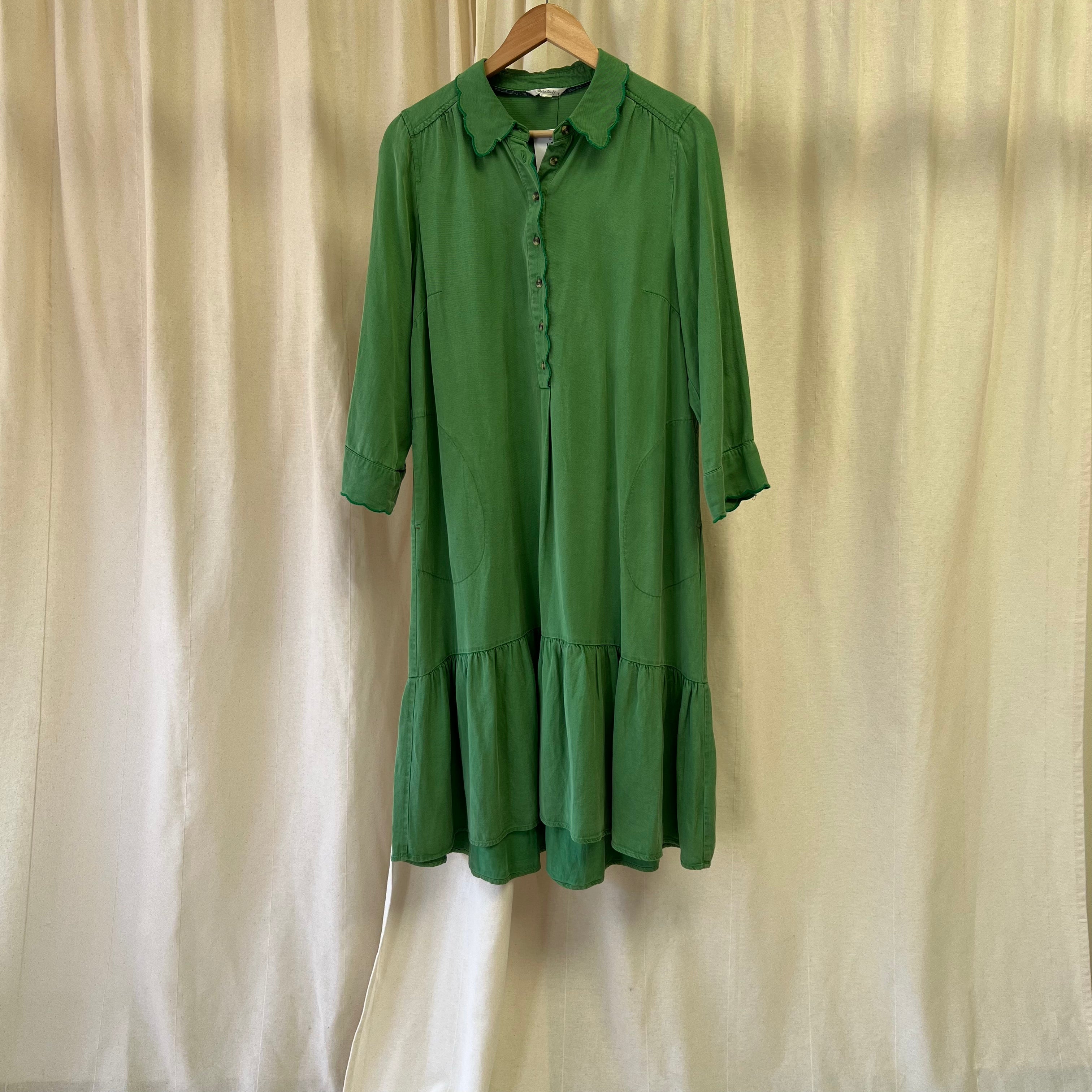 Green dress on a hanger against a beige curtain background