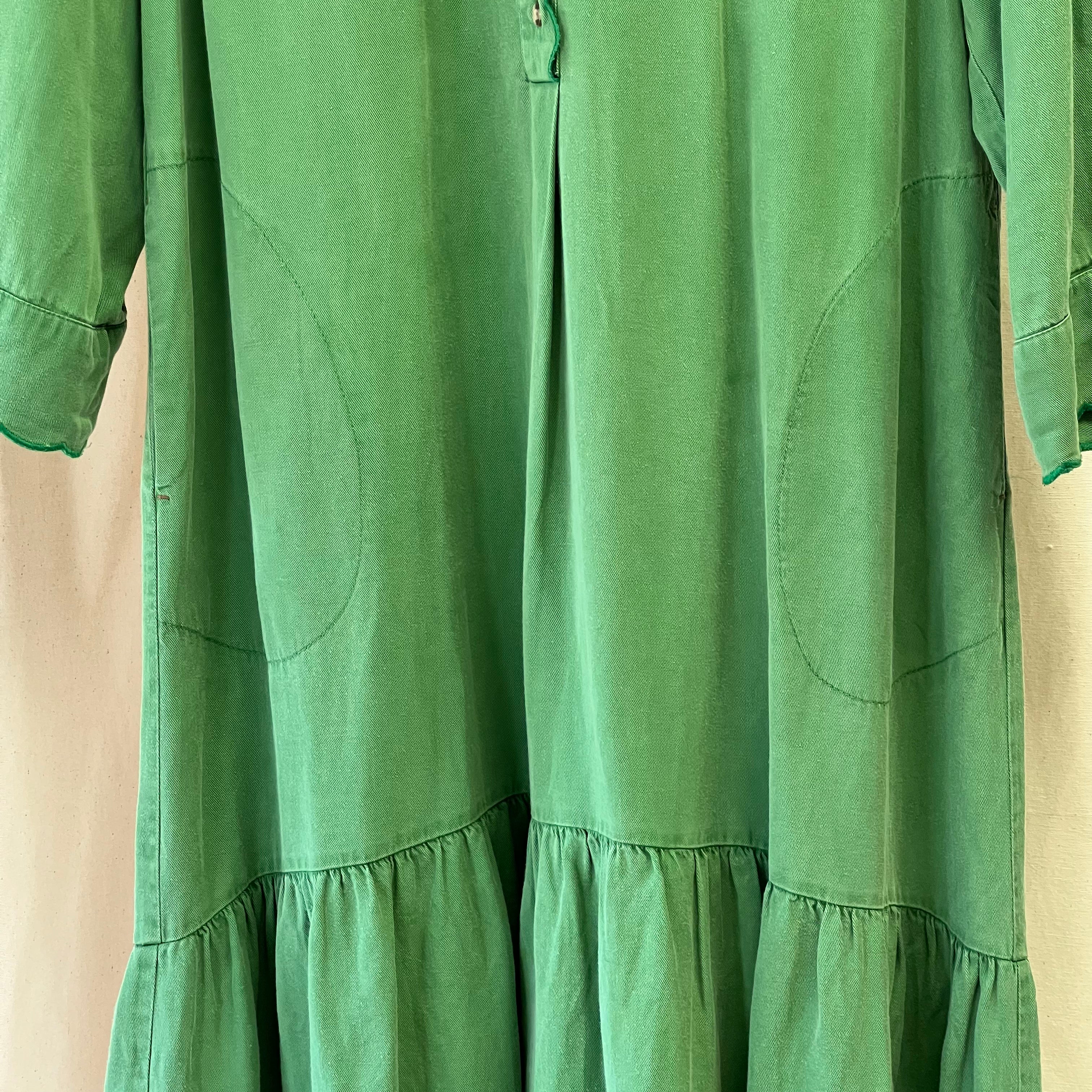 Green dress with long sleeves and a tiered skirt on a beige background