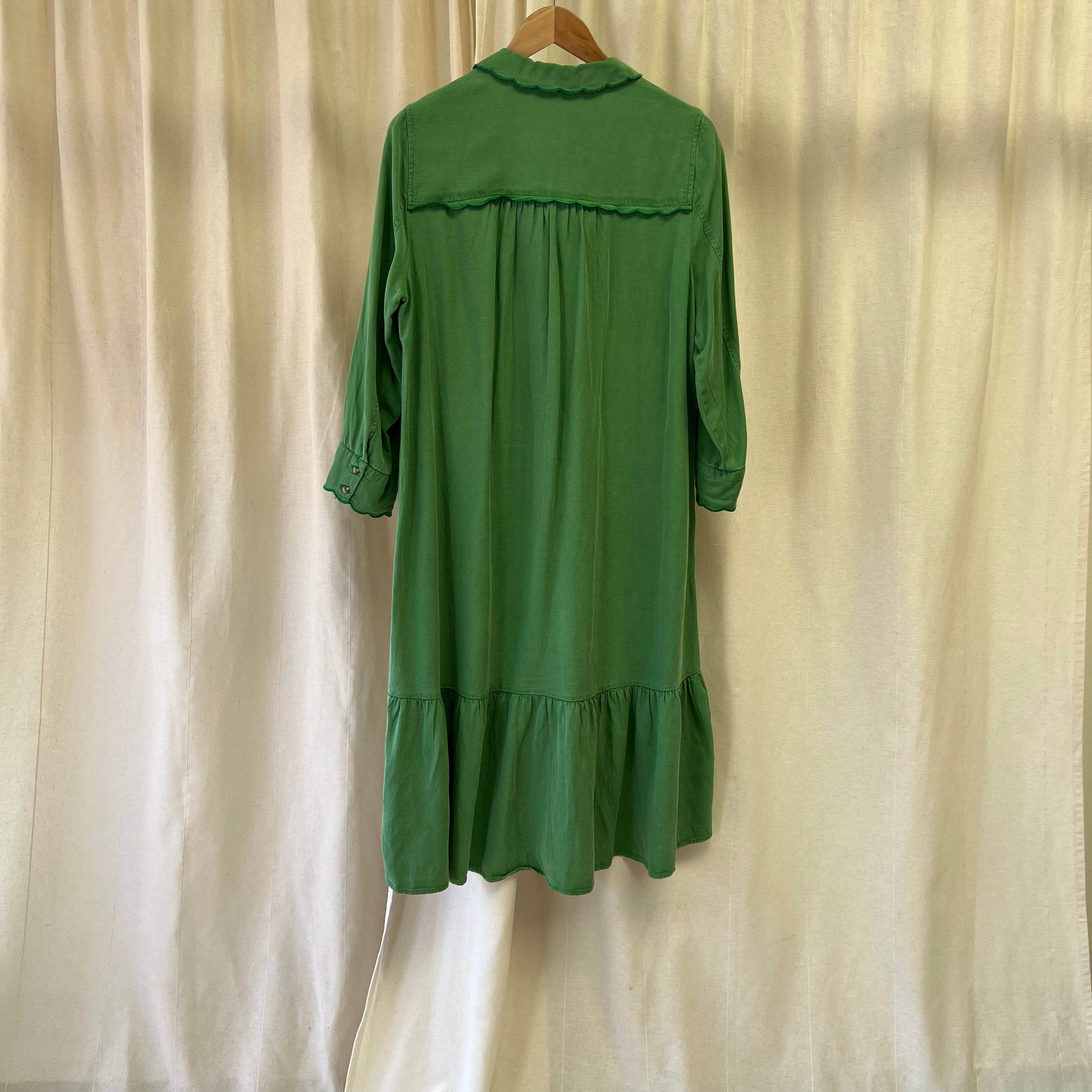 Green dress on a hanger against a beige curtain background