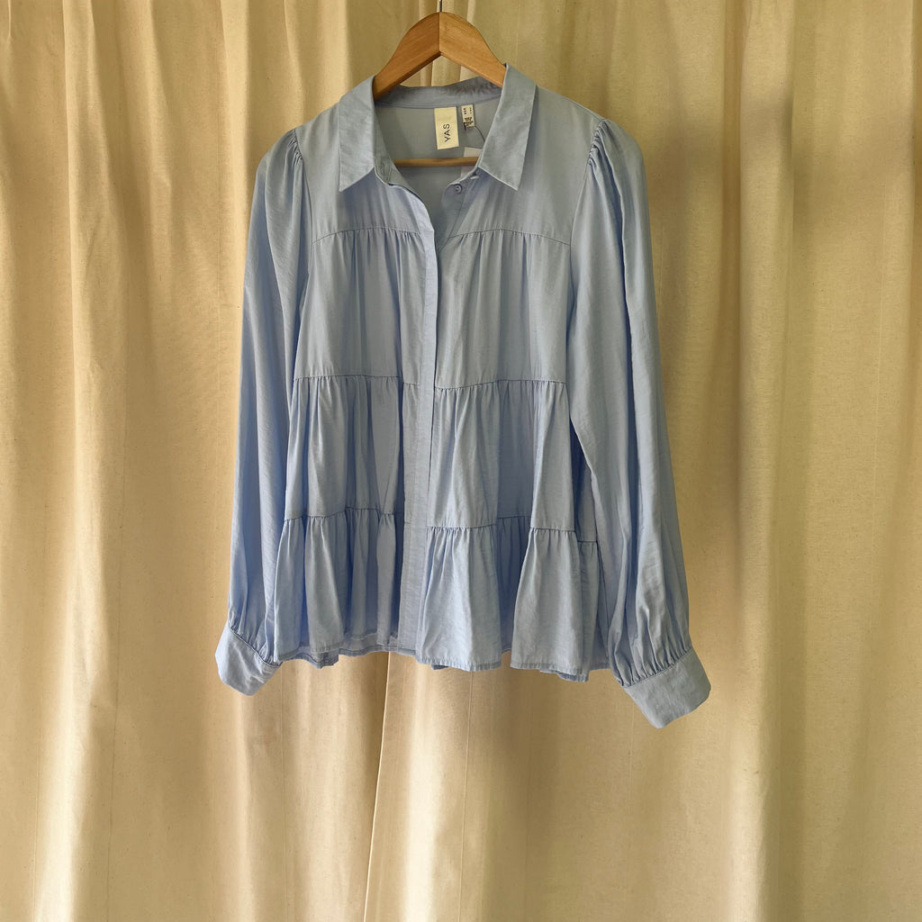 Light blue shirt on a wooden hanger against a beige curtain background