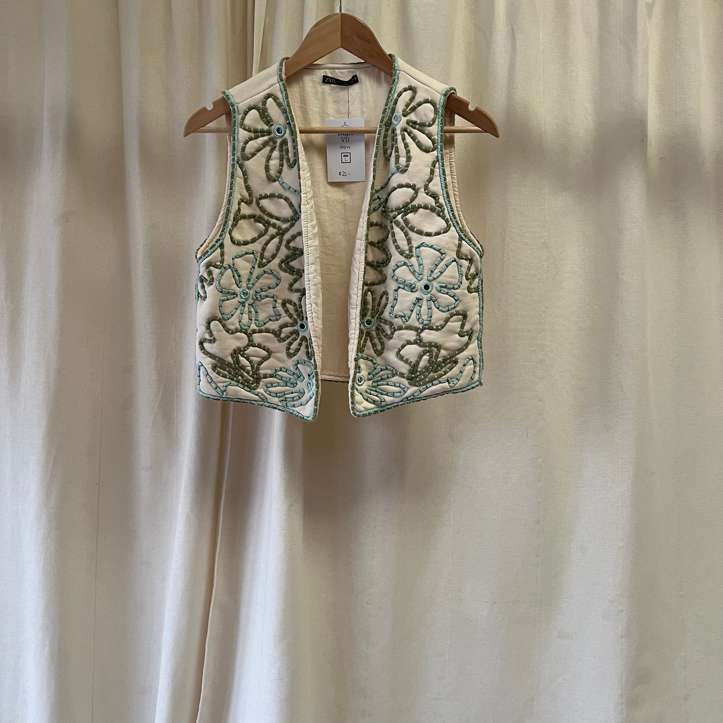 Embroidered vest on a hanger against a plain background