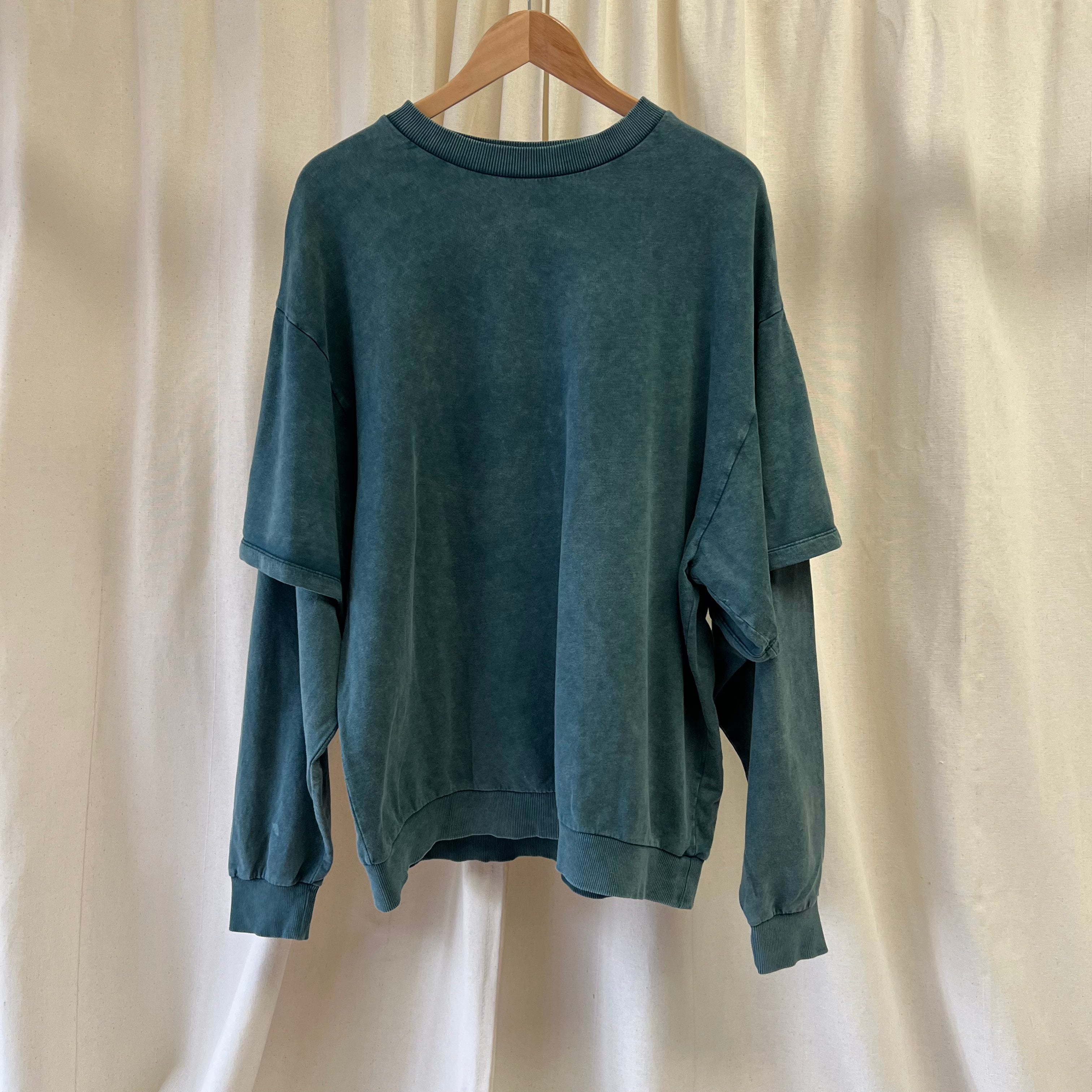 Green sweatshirt on a wooden hanger against a beige curtain background